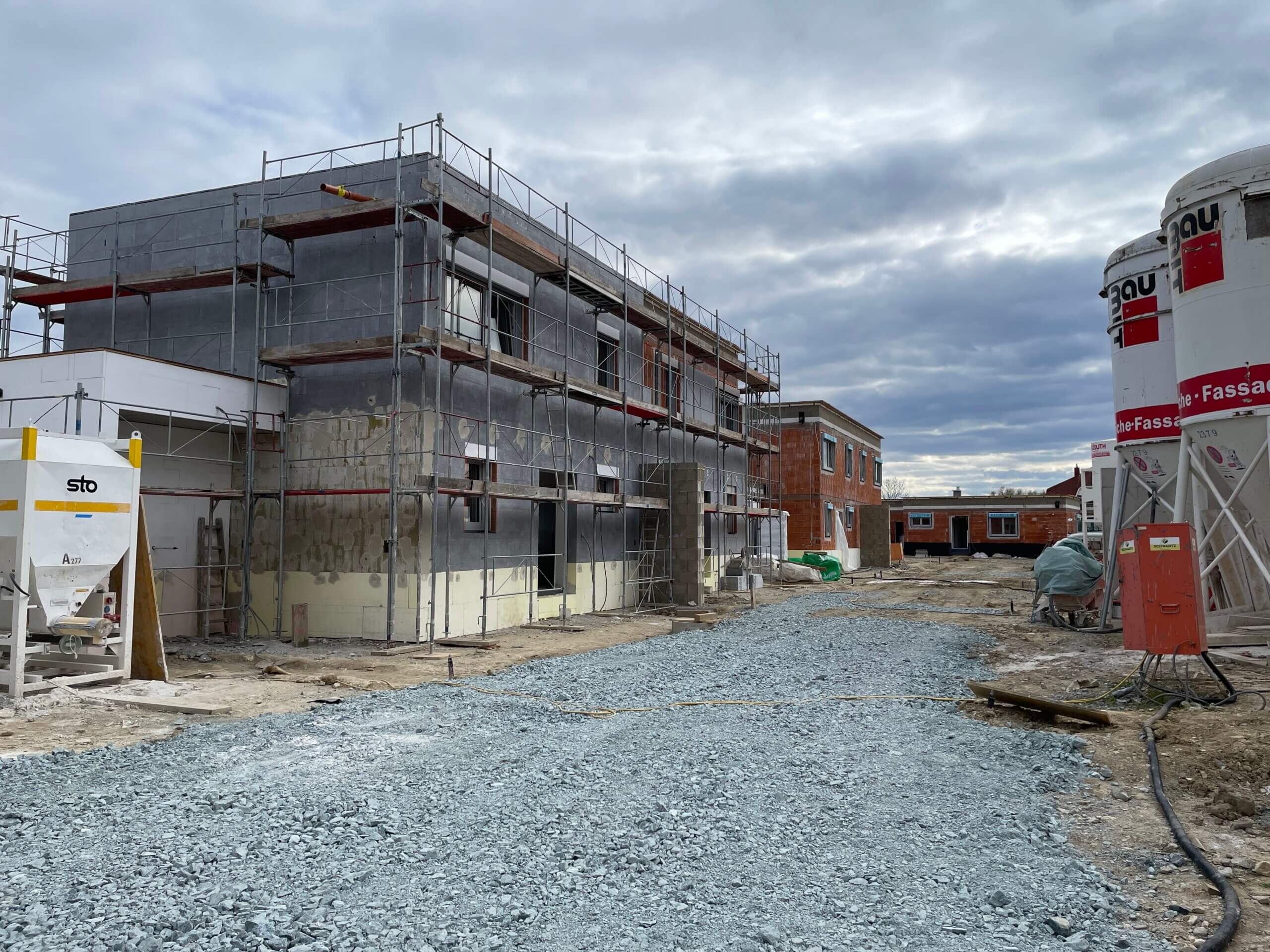 Baustelle: Rohbau eines Hauses mit Gerüst und Baumaterialien an einem bewölkten Tag. Ideal für Bauunternehmen.