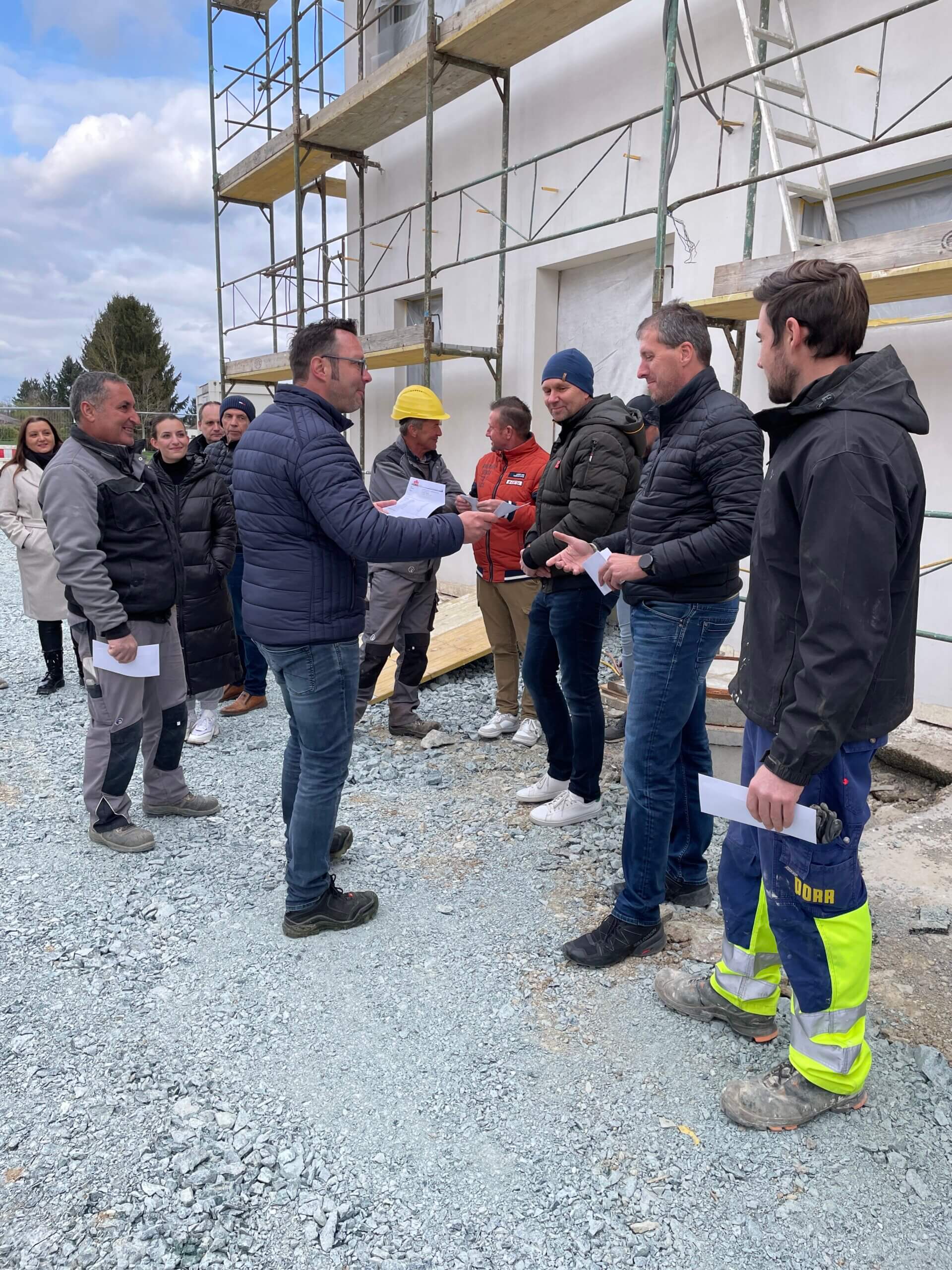 Baustellenbesprechung: Gruppe von Arbeitern und Managern diskutiert Bauprojekt vor einem eingerüsteten Gebäude.