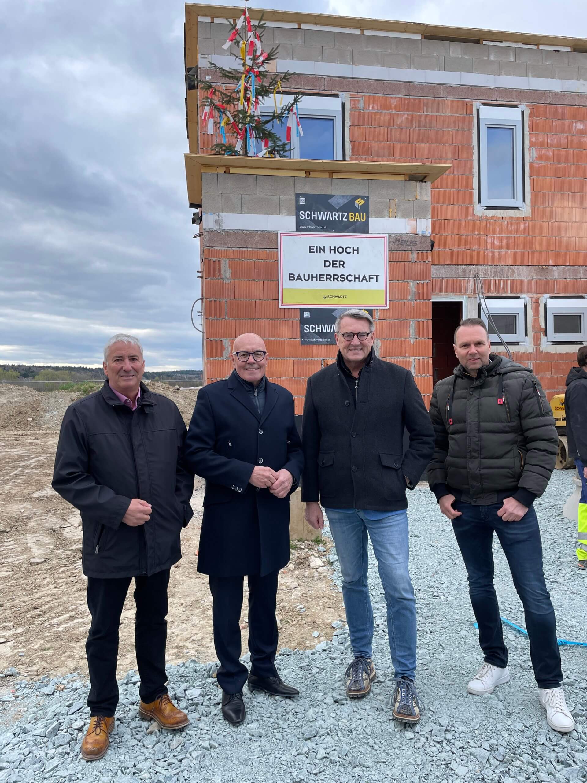 Gruppe vor Rohbau mit Richtkranz und Schild „Ein Hoch der Bauherrschaft“ bei Schwartz Bau.