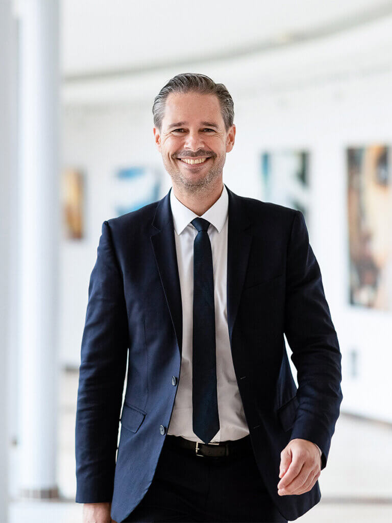 Mann im Anzug lächelt selbstbewusst und geht in einem modernen Bürogebäude, Geschäftsmann-Konzept.
