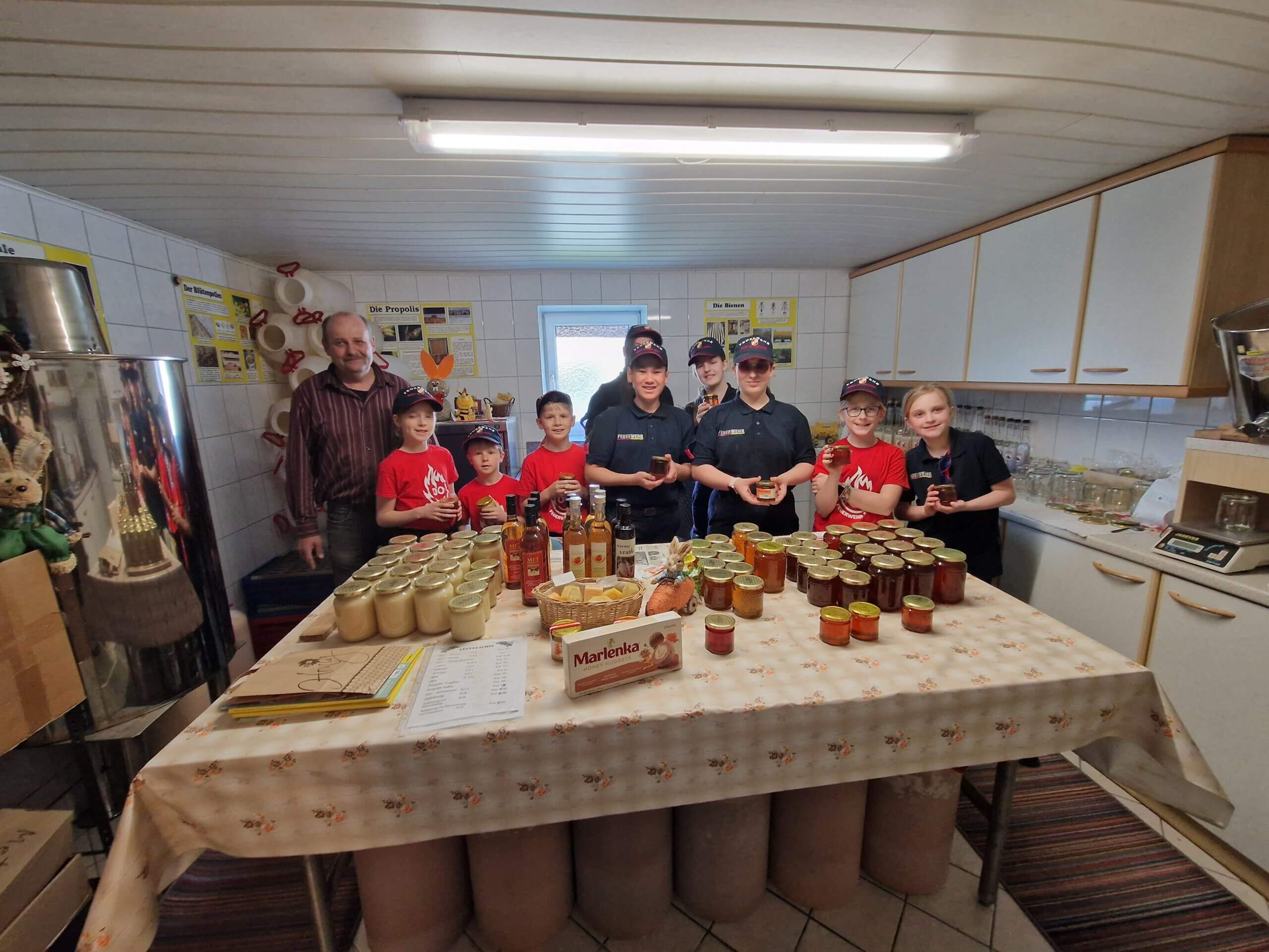 Gruppe in Imkerei zeigt Honiggläser und Produkte auf einem Tisch in einer Werkstatt.