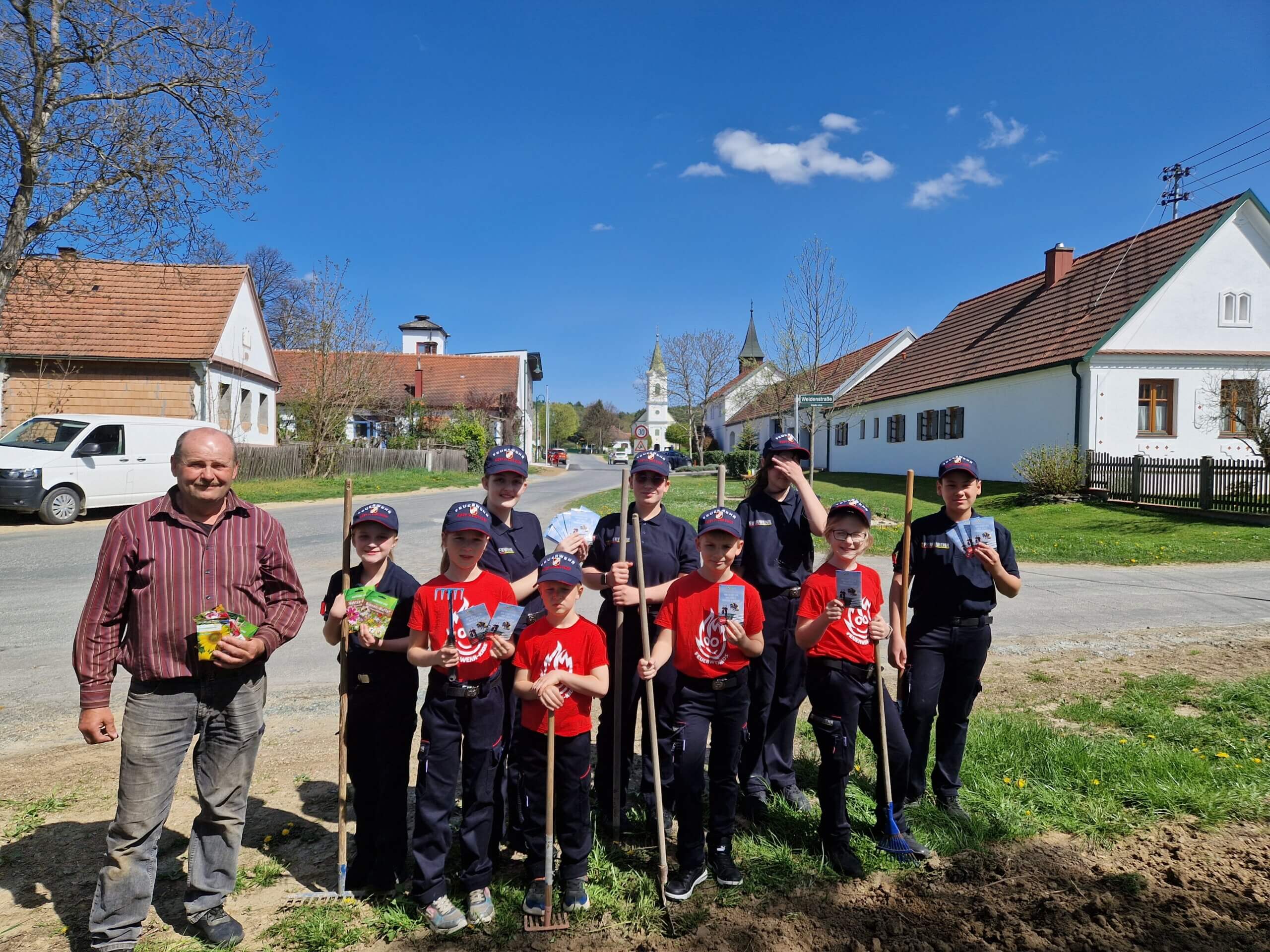 Gruppe Jugendlicher pflanzt unter blauem Himmel mit einem Erwachsenen in einem Dorf gemeinsam Pflanzen.