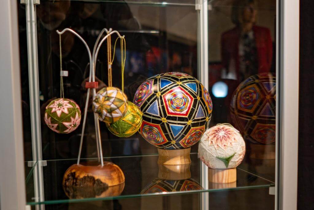 Ausstellung von bunten, handgefertigten Temari-Bällen in einer Vitrine, verschiedene Designs und Größen sichtbar.