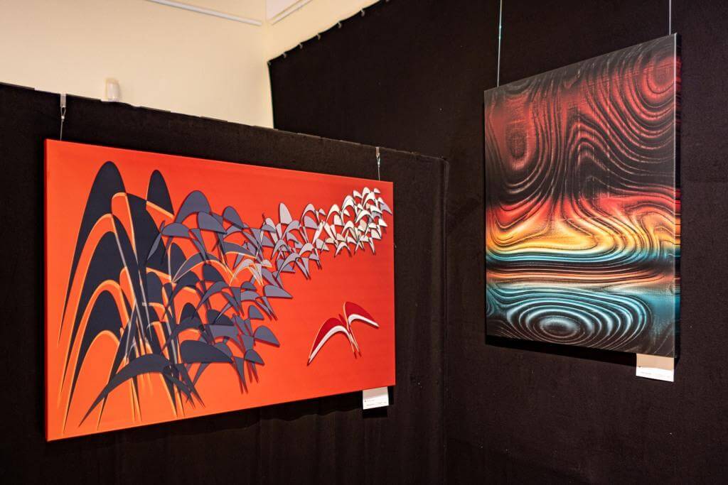 Moderne Kunstgalerie mit abstrakten Gemälden: links Vögel in Bewegung, rechts farbenfrohe, wellenartige Formen.