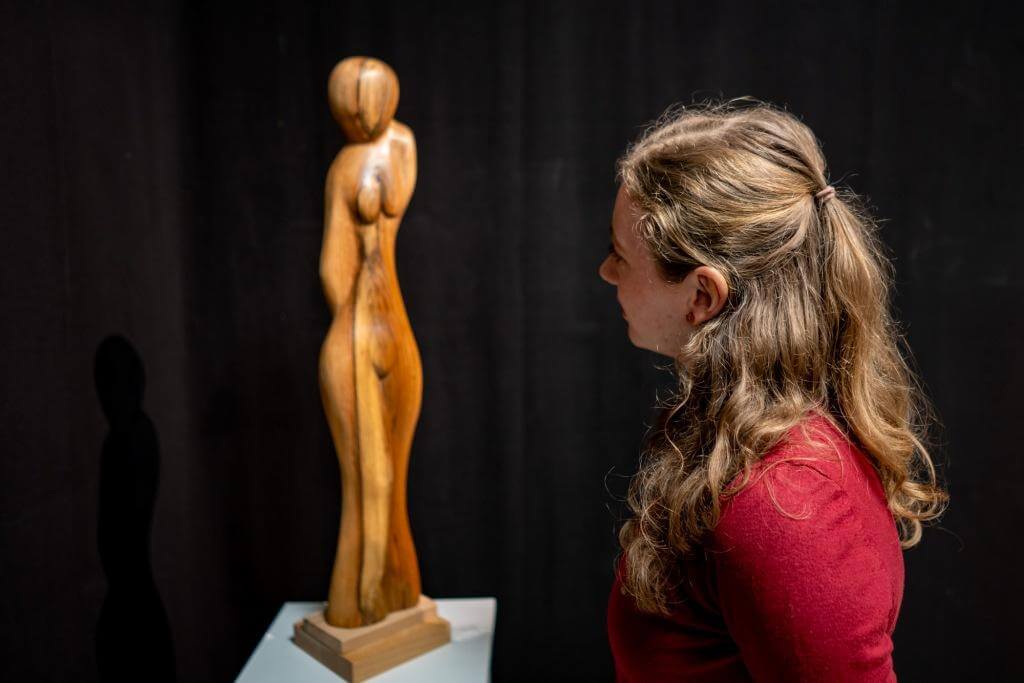 Frau betrachtet eine abstrakte Holzskulptur in einer Galerie. Kunstinteresse, Skulptur, Ausstellung.