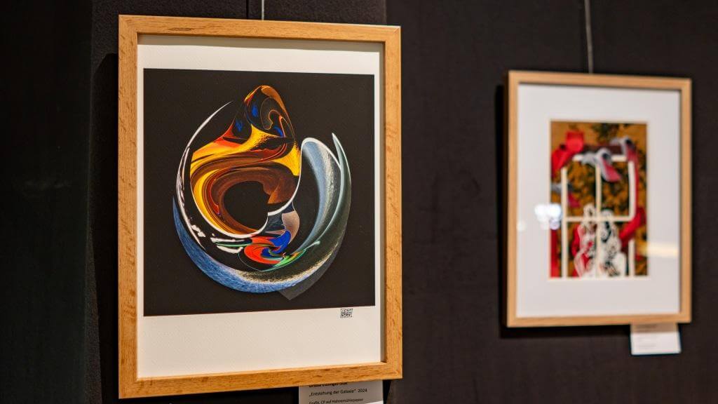 Zwei gerahmte abstrakte Kunstwerke an einer dunklen Ausstellungswand in einer modernen Galerie.