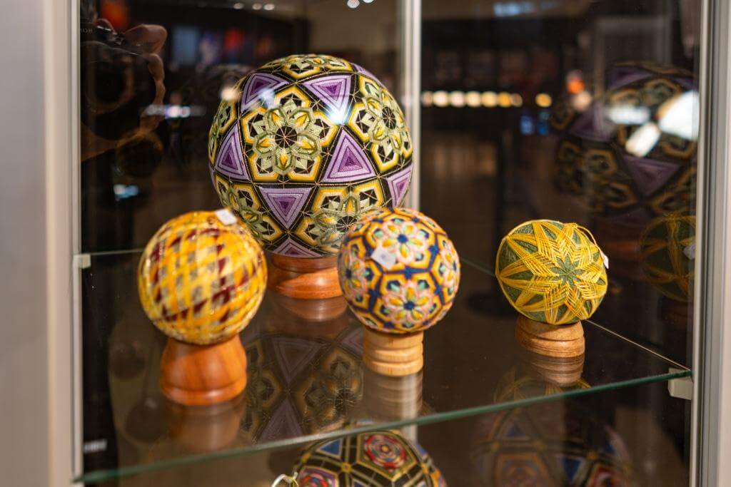 Kunstvoll gestaltete Temaribälle in einer Glasvitrine, präsentiert in unterschiedlichen Farben und Mustern.