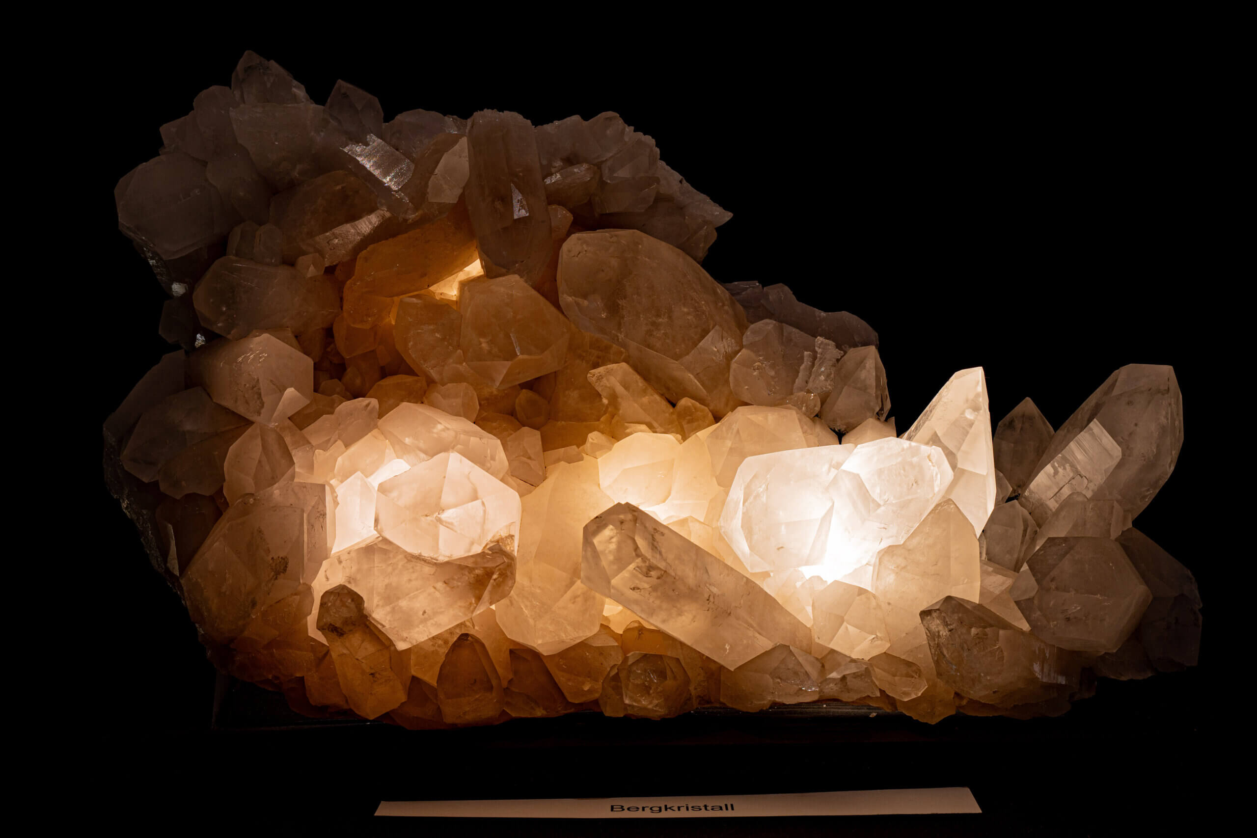 Leuchtender Bergkristallcluster vor schwarzem Hintergrund, zeigt Naturwunder und brillante Kristallstrukturen.