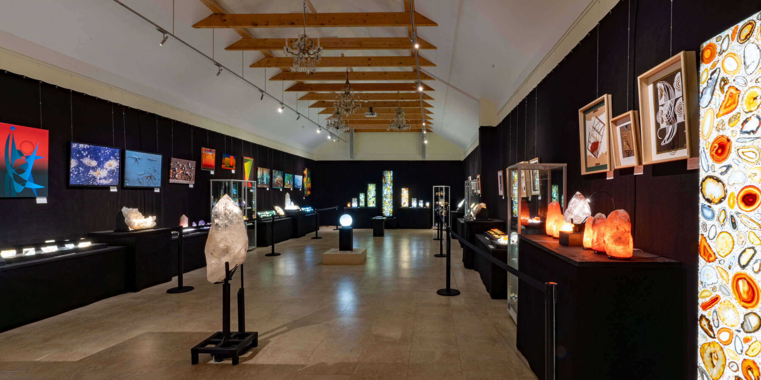 Kunstgalerie mit beleuchteten Kristallen und Gemälden, modern präsentiert vor schwarzem Hintergrund in einem Ausstellungsraum.