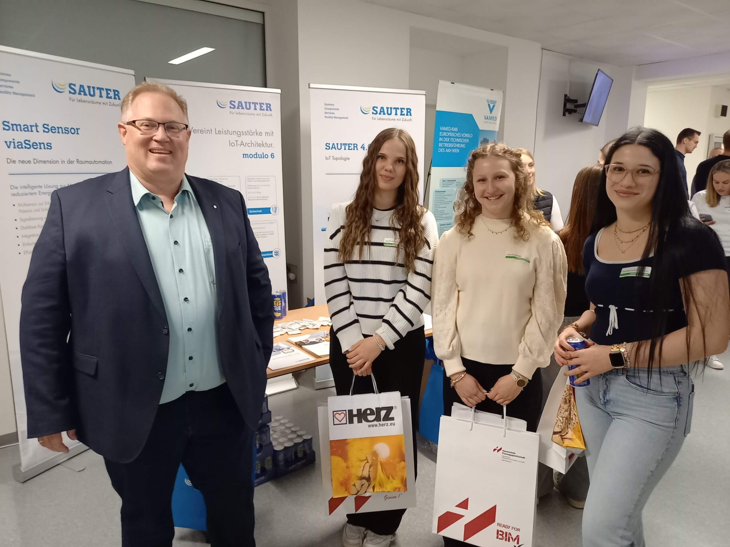 Gruppe von Menschen bei einer Messe, posierend vor einem Stand von Sauter mit Informationspostern im Hintergrund.