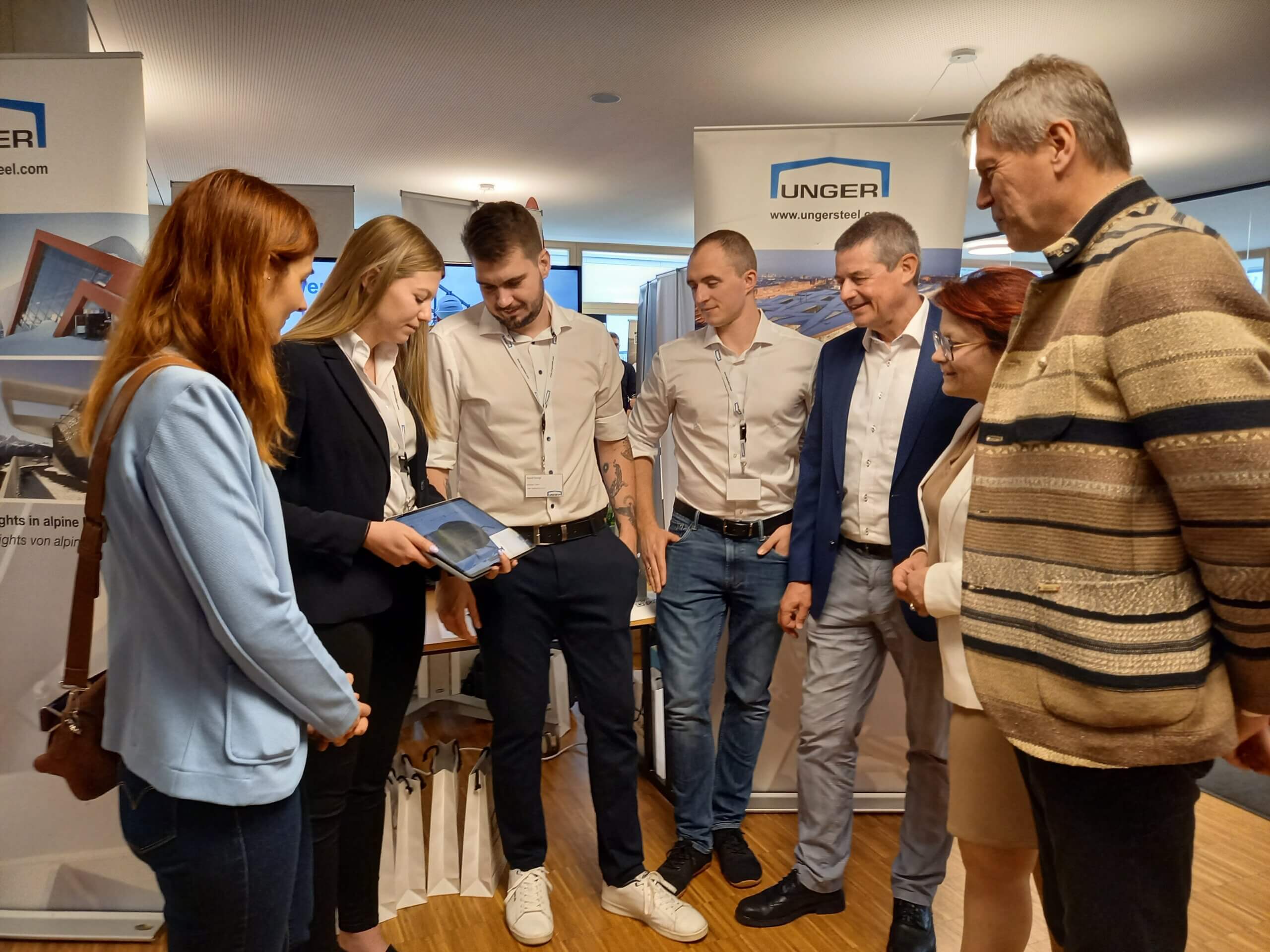 Gruppe von Geschäftsleuten bei einer Präsentation mit Tablet, vor UNGER-Logos, in einem modernen Büro.