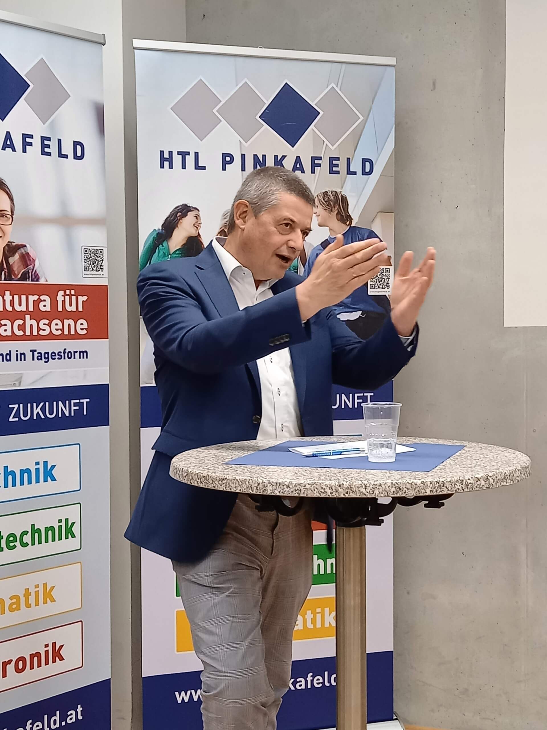 Ein Mann hält einen Vortrag an der HTL Pinkafeld vor Roll-ups mit Bildungsangeboten.