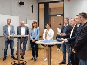 Gruppe von Personen in Geschäftskleidung bei einem Stehempfang, Diskussion in modernem Konferenzraum.