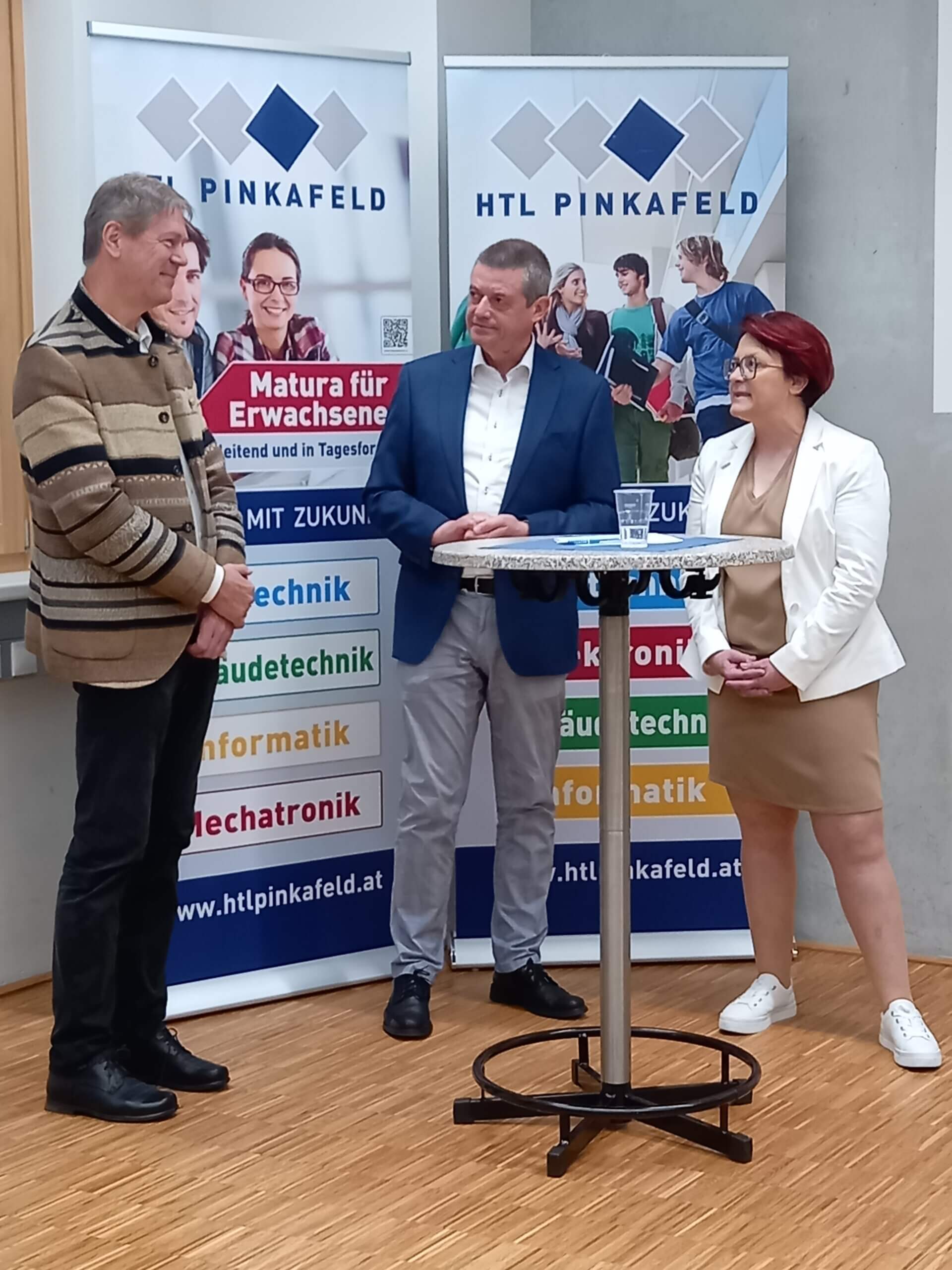 Drei Personen stehen vor HTL Pinkafeld Bannern bei einer Veranstaltung.