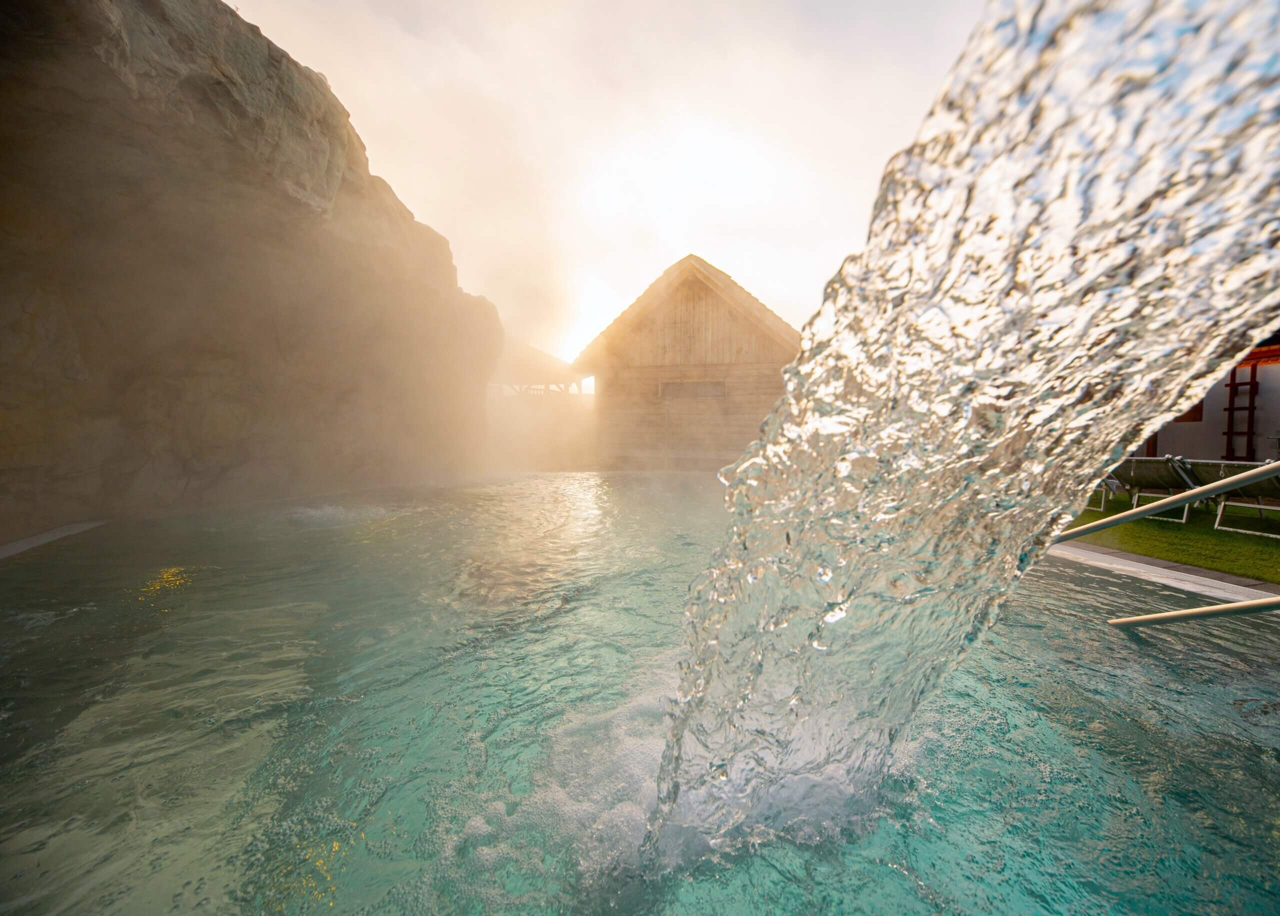 Thermalquelle bei Sonnenuntergang, sprudelndes warmes Wasser in entspannter Wellness-Landschaft.