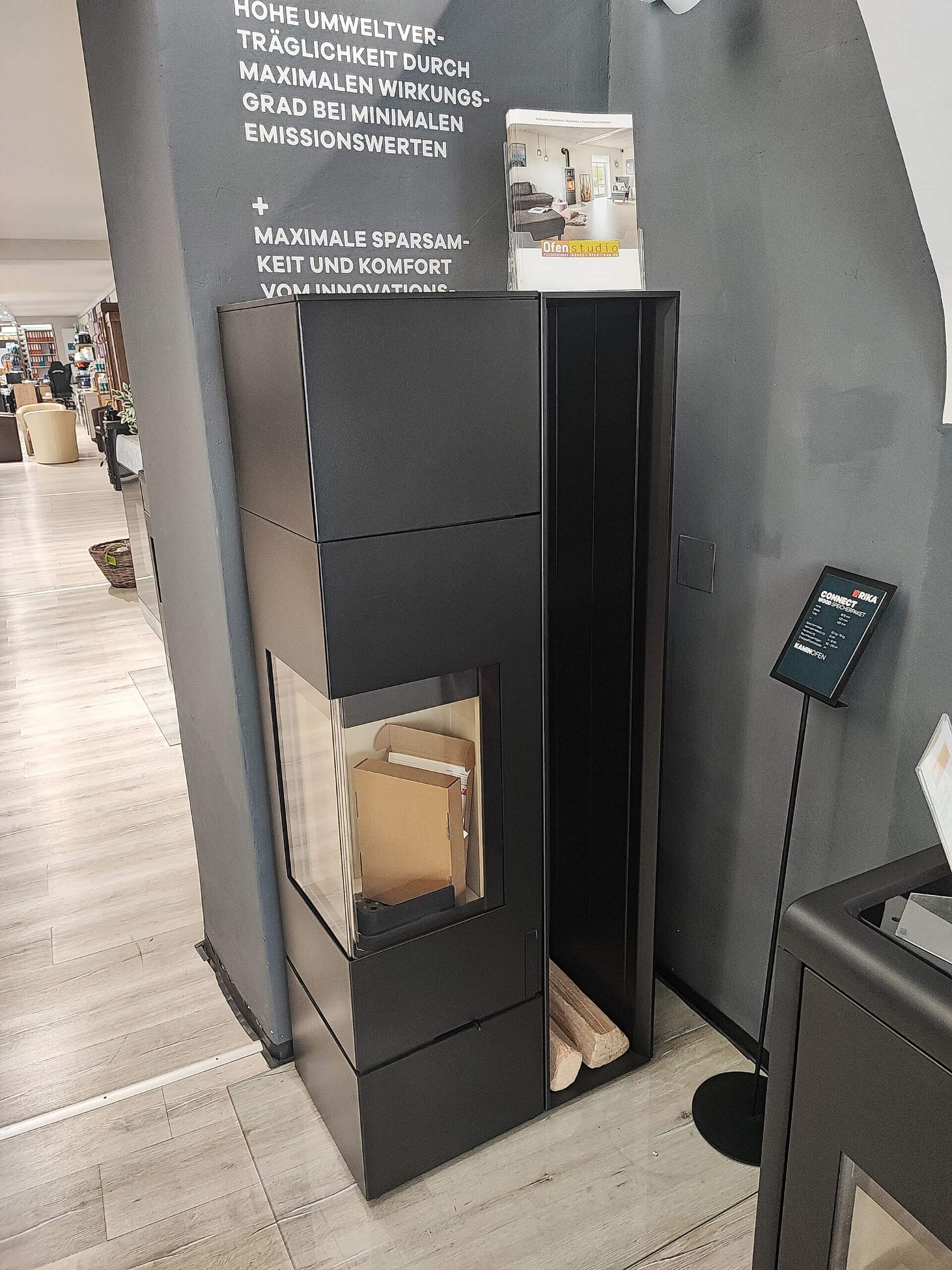 Moderner schwarzer Kaminofen mit Glasfenster in einem Ausstellungsraum, ideal für effizientes und stilvolles Heizen.