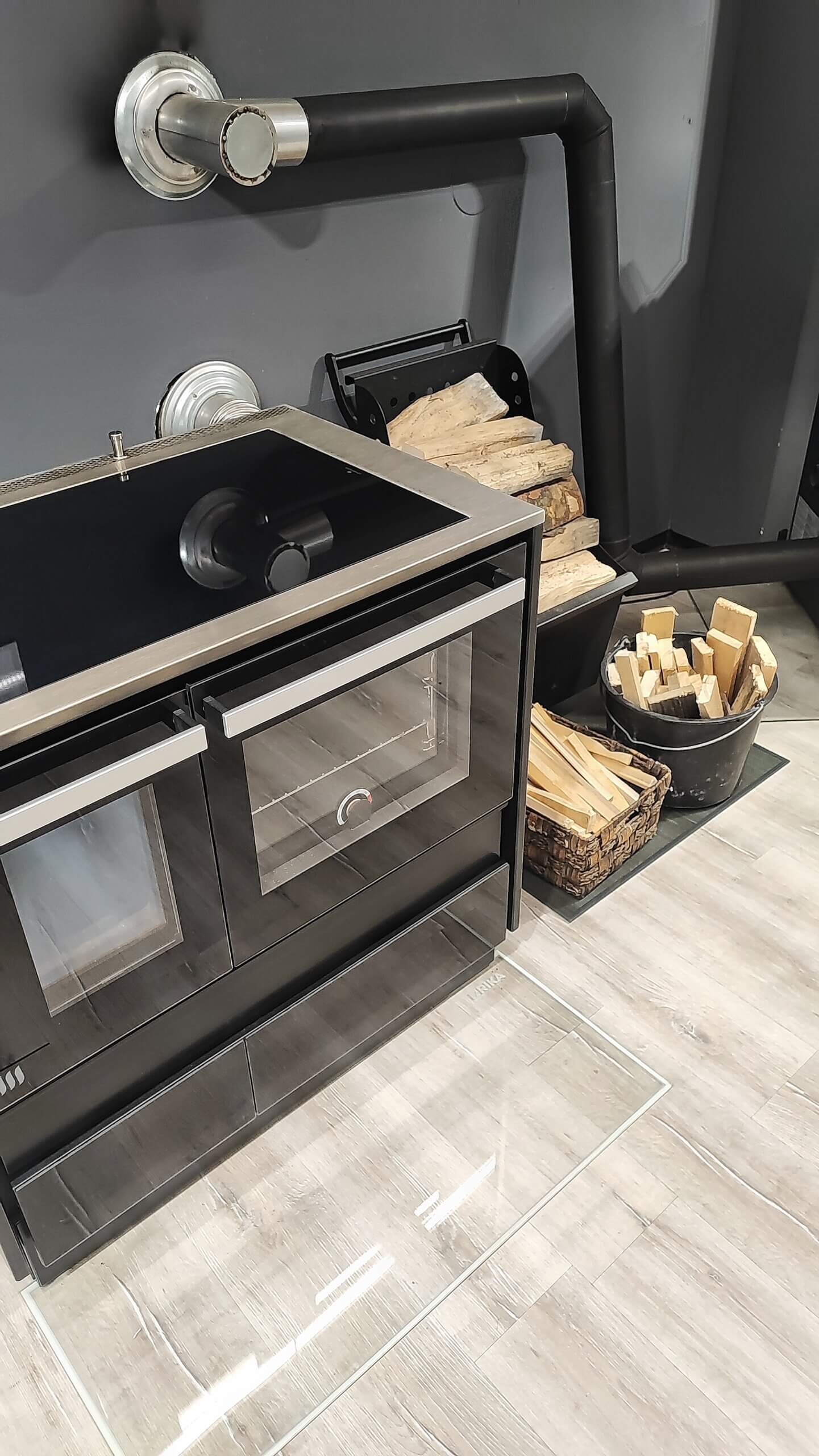 Moderner Kaminofen mit Holzscheiten, schwarzem Rohr und gläserner Backofentür in stilvollem Raum. Optimal für Wärme und Design.