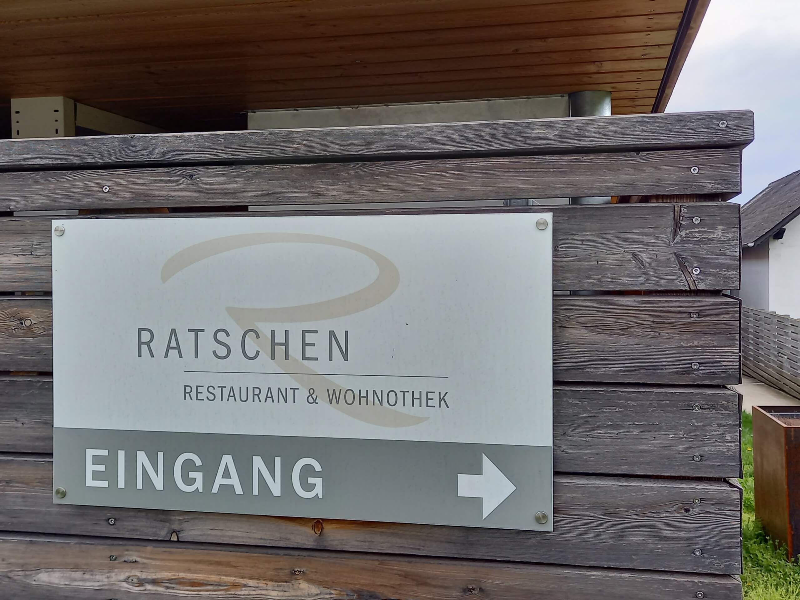 Eingangsschild des Ratschen Restaurant & Wohnothek auf Holz, mit Pfeil, der nach rechts zeigt.