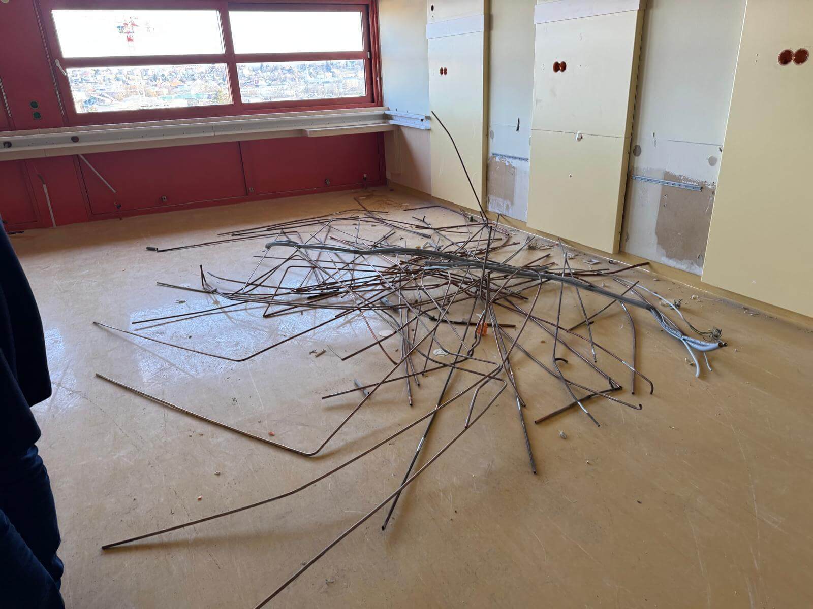 Alttext: Leerer Raum mit Fenster, Haufen Metallstangen auf dem Boden, teils freigelegte Wandpaneele.