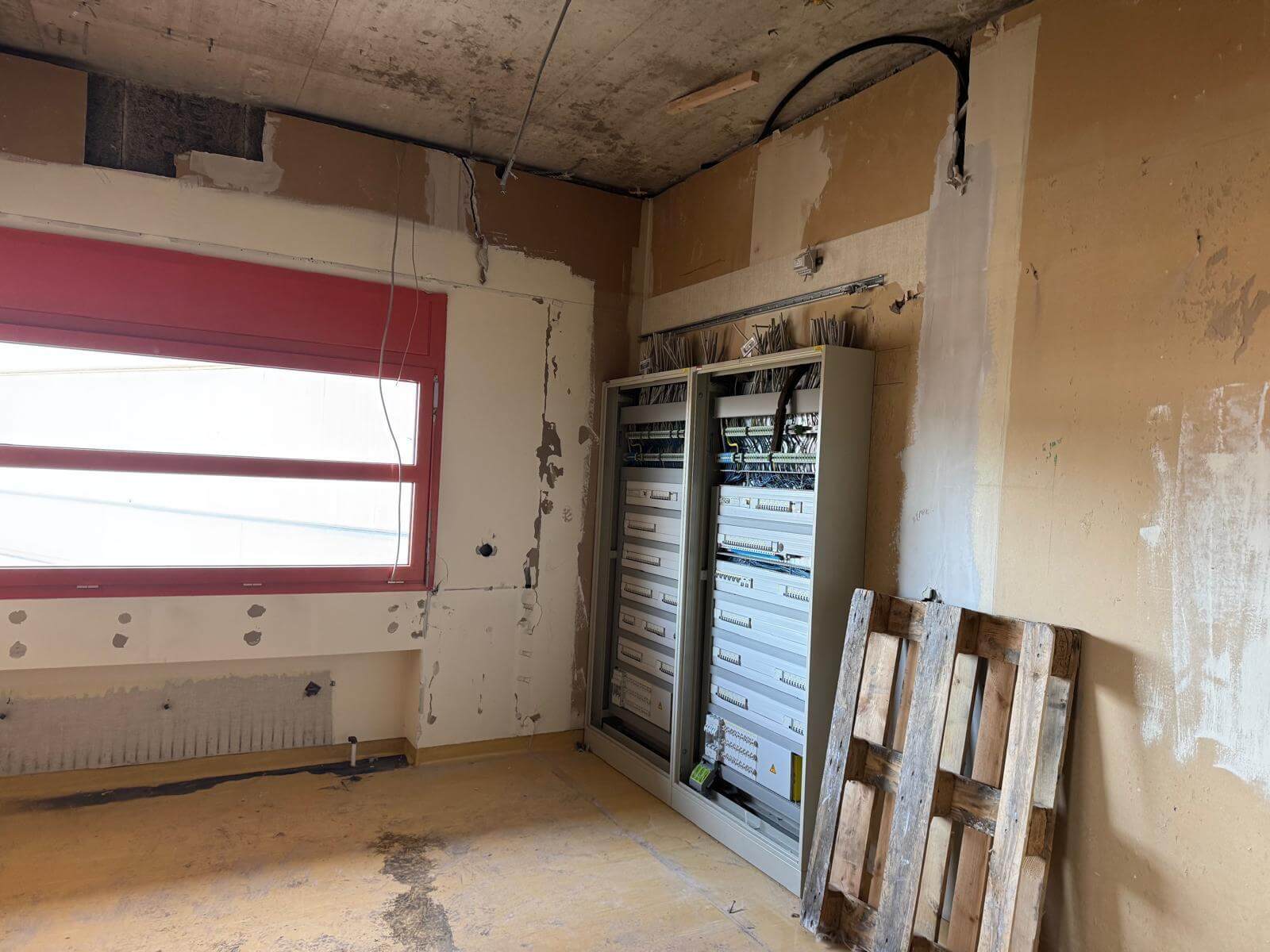 Renovierungsbedarf im Raum mit Verteilerkasten und Fenster, Baustelle zeigt unfertige Wände und Kabelinstallation.