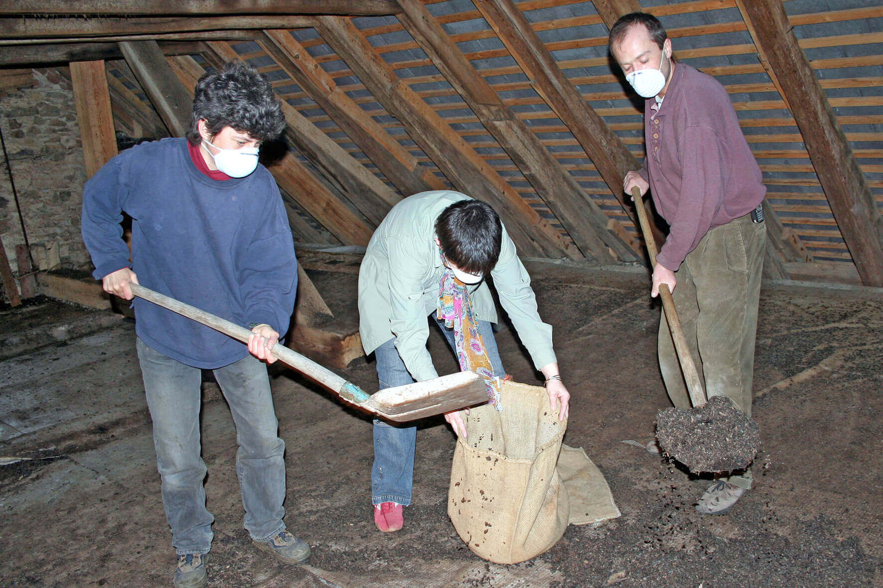 Personen mit Masken kompostieren Erde auf einem Dachboden, sie befüllen Säcke. Umweltfreundliche Gartenarbeit.