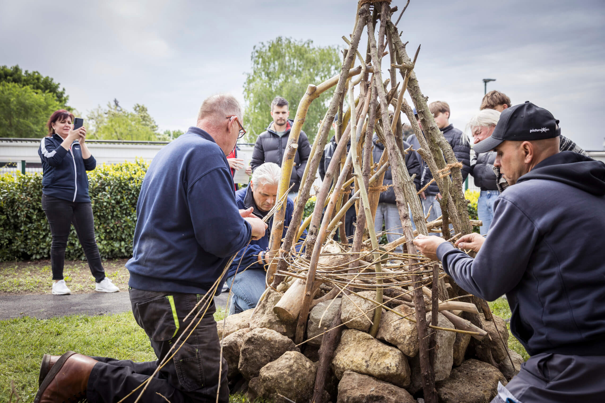 Personen bauen gemeinsam eine Holzstruktur im Freien. Workshop zur praktischen Teamarbeit im Grünen.