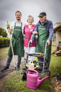 Seniorenpflege im Garten: Betreuerin mit Senioren beim Gärtnern im Freien. Unterstützung und Freude in der Natur.