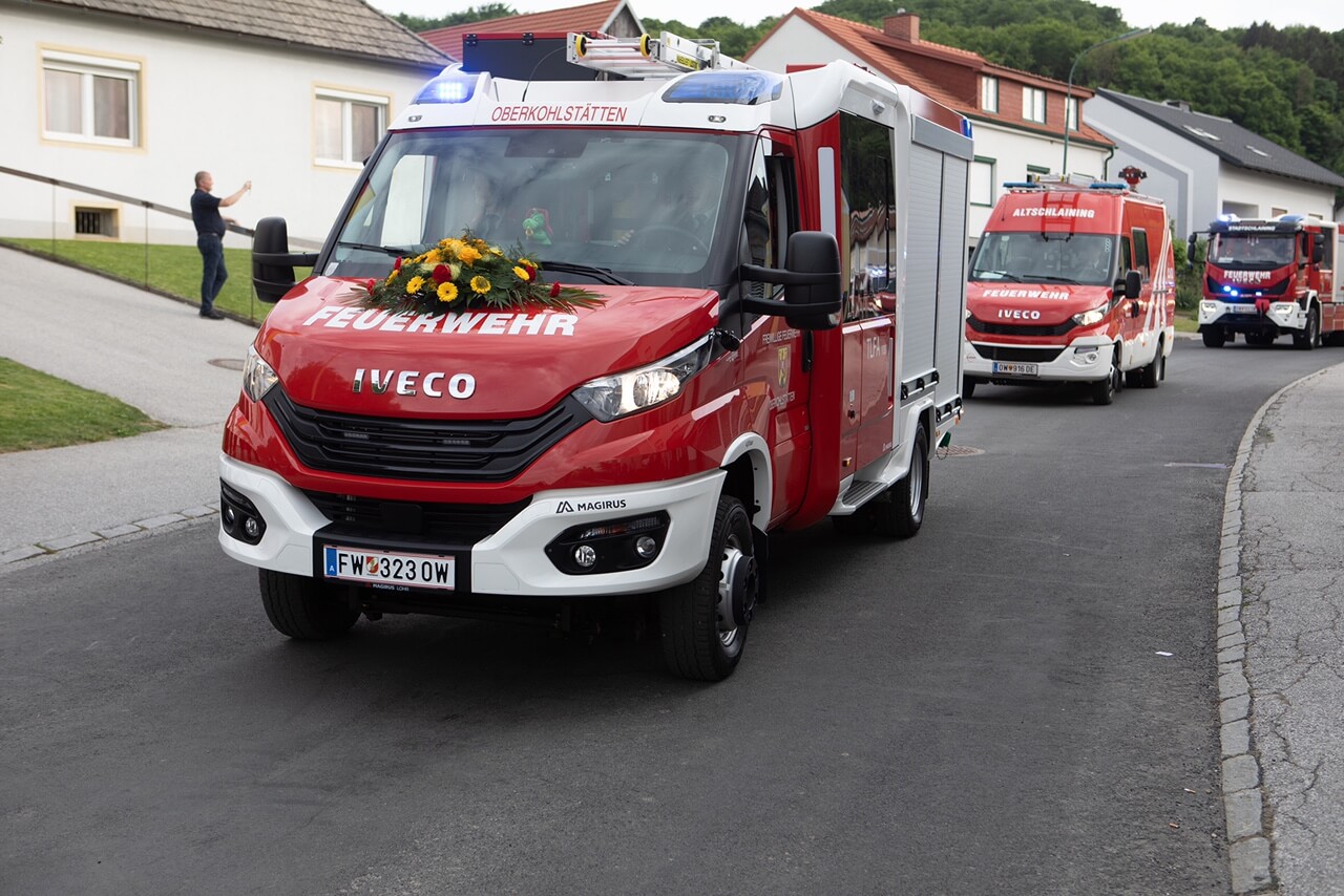 Feuerwehrfahrzeuge parade bei einer Veranstaltung in Oberkohlstätten, Menschen beobachten die Szene am Straßenrand.