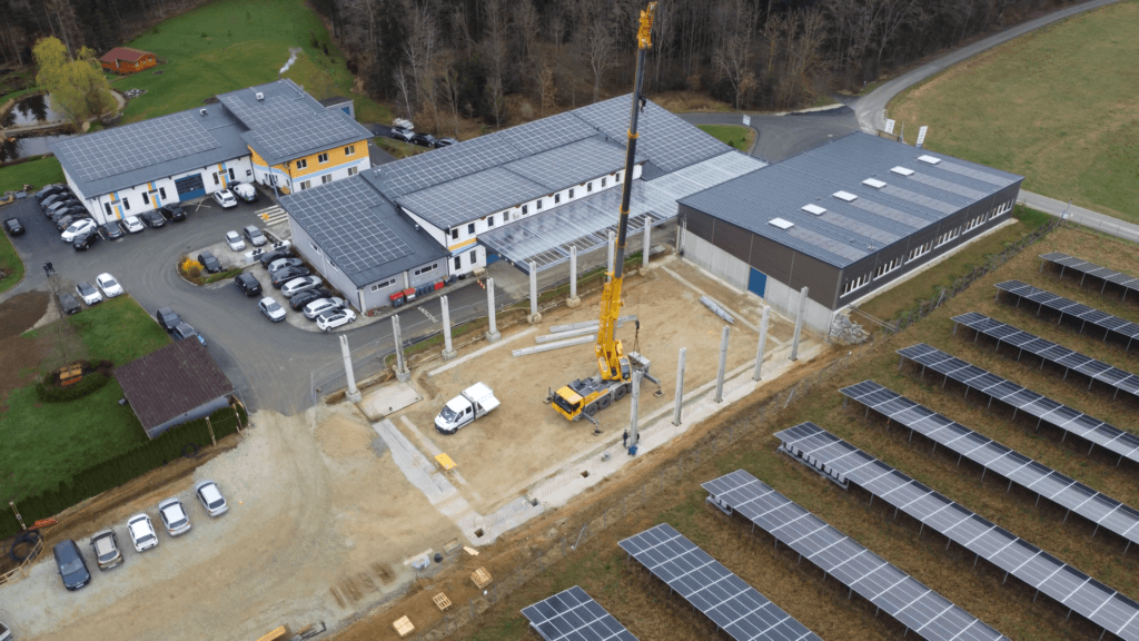 Hallenbau1 Luftaufnahme eines Bauprojekts mit Solaranlagen, Kran und Gebäuden in grüner Umgebung.