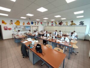 Schüler in weißen Kitteln arbeiten konzentriert in einem farbenfrohen Chemie-Klassenzimmer mit Wanddekorationen.