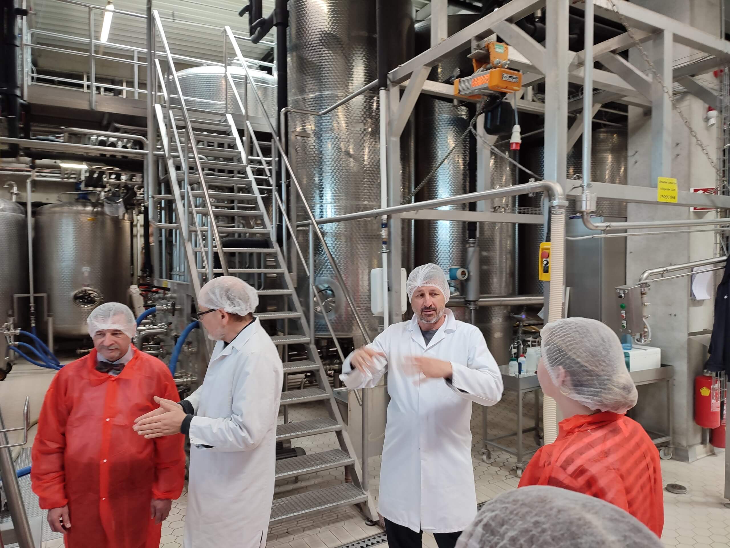 Besichtigung einer industriellen Produktionsanlage mit Mitarbeitern in Schutzkleidung und Besprechung vor Edelstahltanks.