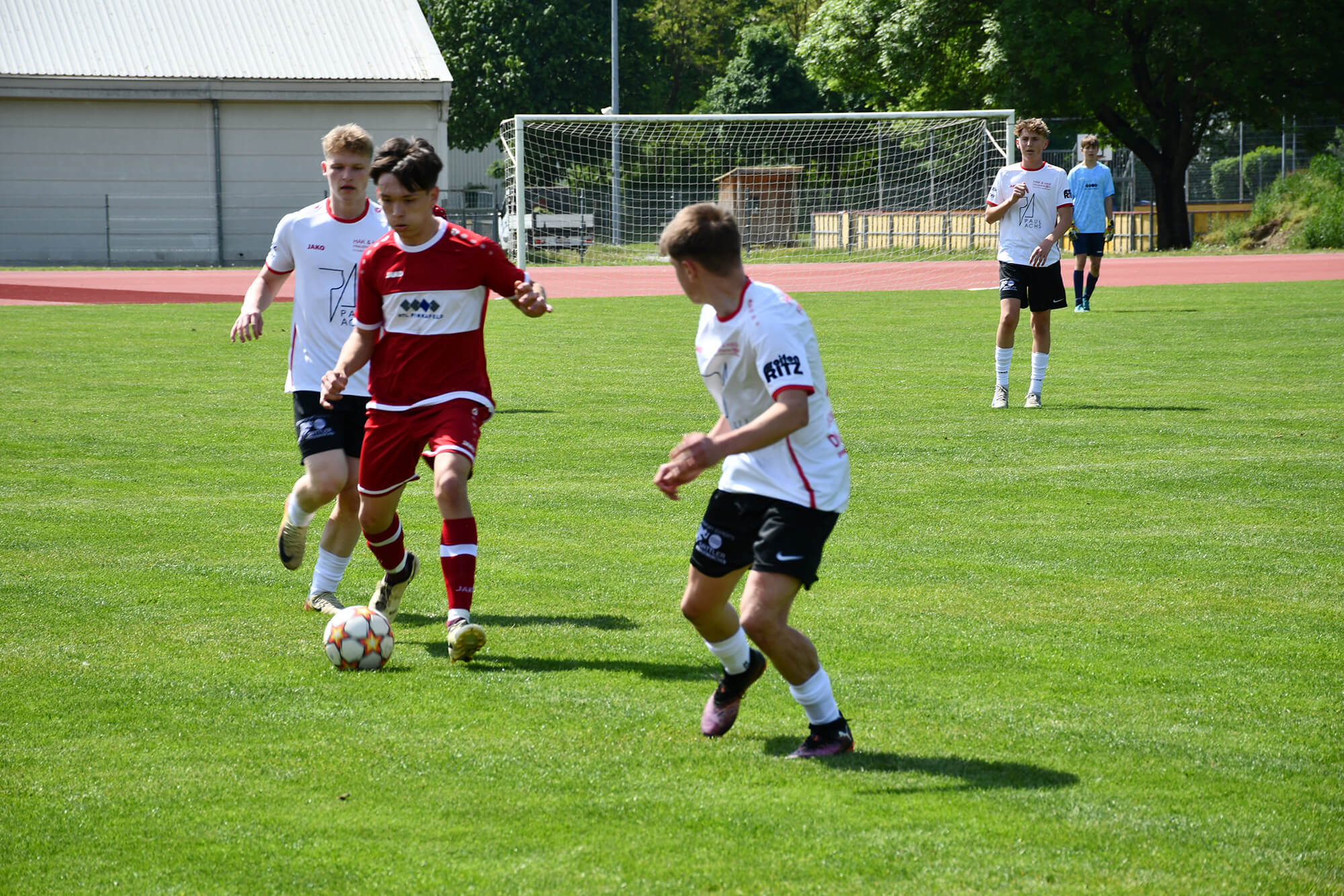 Jugendfußballspiel: Spieler im roten Trikot dribbelt auf dem Spielfeld, verfolgt von Gegenspielern in weißen Trikots.