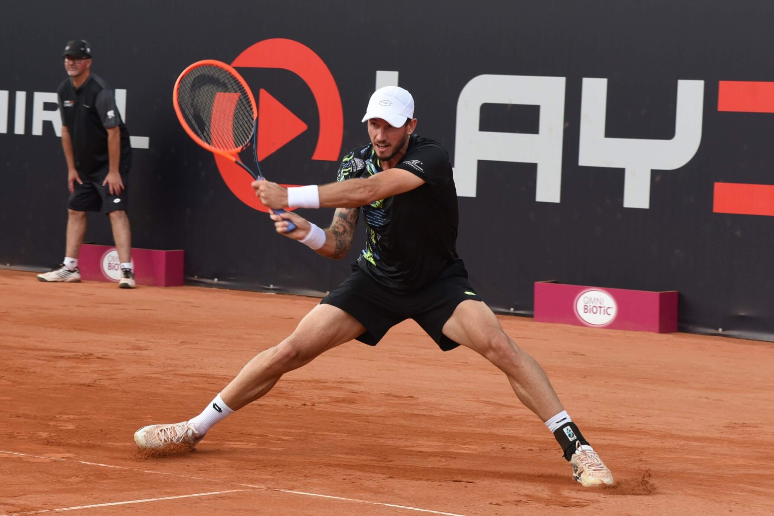 Tennisspieler führt einen Rückhand-Volley auf dem Sandplatz aus, intensives Match unter freiem Himmel.