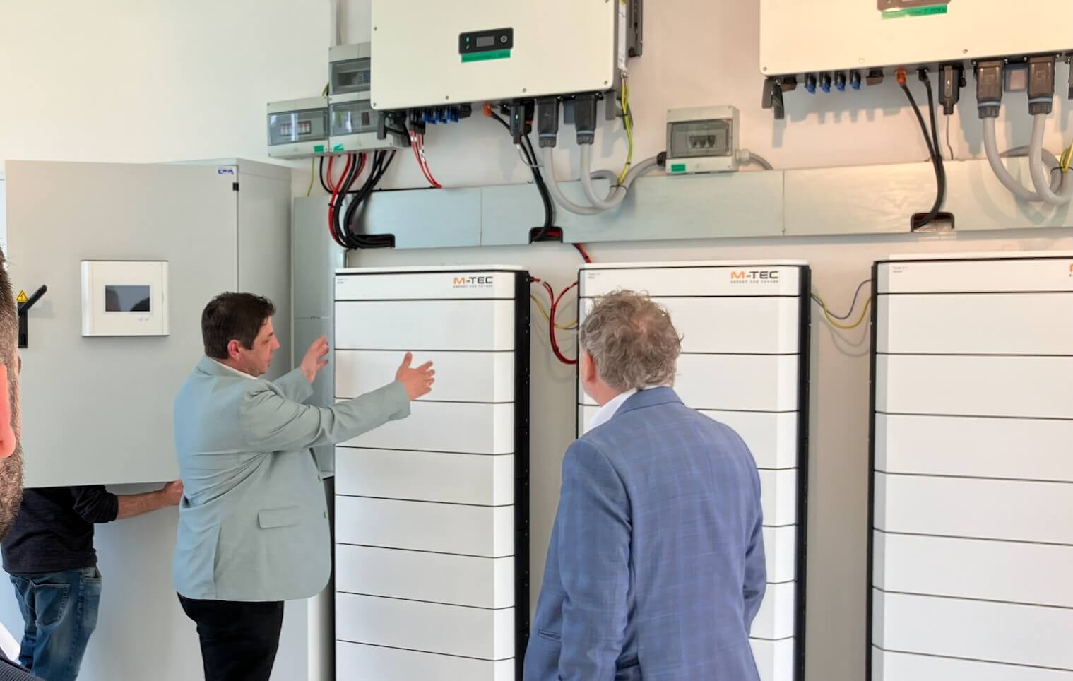 Personen diskutieren vor modernen Energiespeichersystemen in einem technischen Raum.