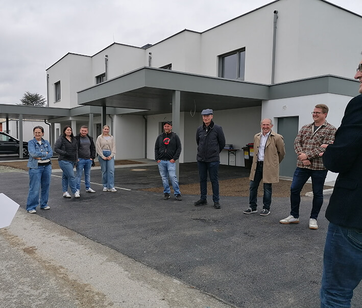 Gruppe von Menschen steht vor einem modernen Gebäude auf einem Parkplatz.