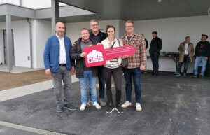 Gruppe von Menschen bei einer Hausübergabe, hält symbolischen Schlüssel mit OSG Logo in Burgenland.