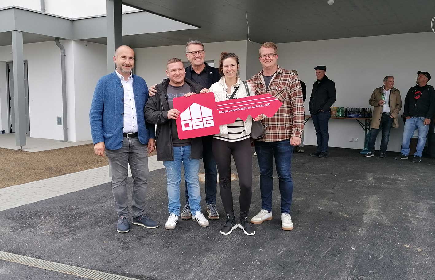 Gruppe von Menschen bei einer Hausübergabe, hält symbolischen Schlüssel mit OSG Logo in Burgenland.
