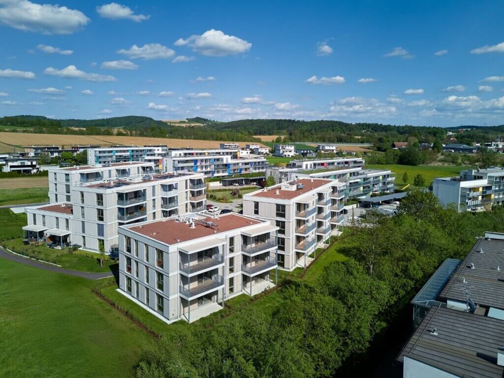 Moderne Wohnanlage in grüner Umgebung mit mehreren Mehrfamilienhäusern und blauen Himmel, Vogelperspektive.