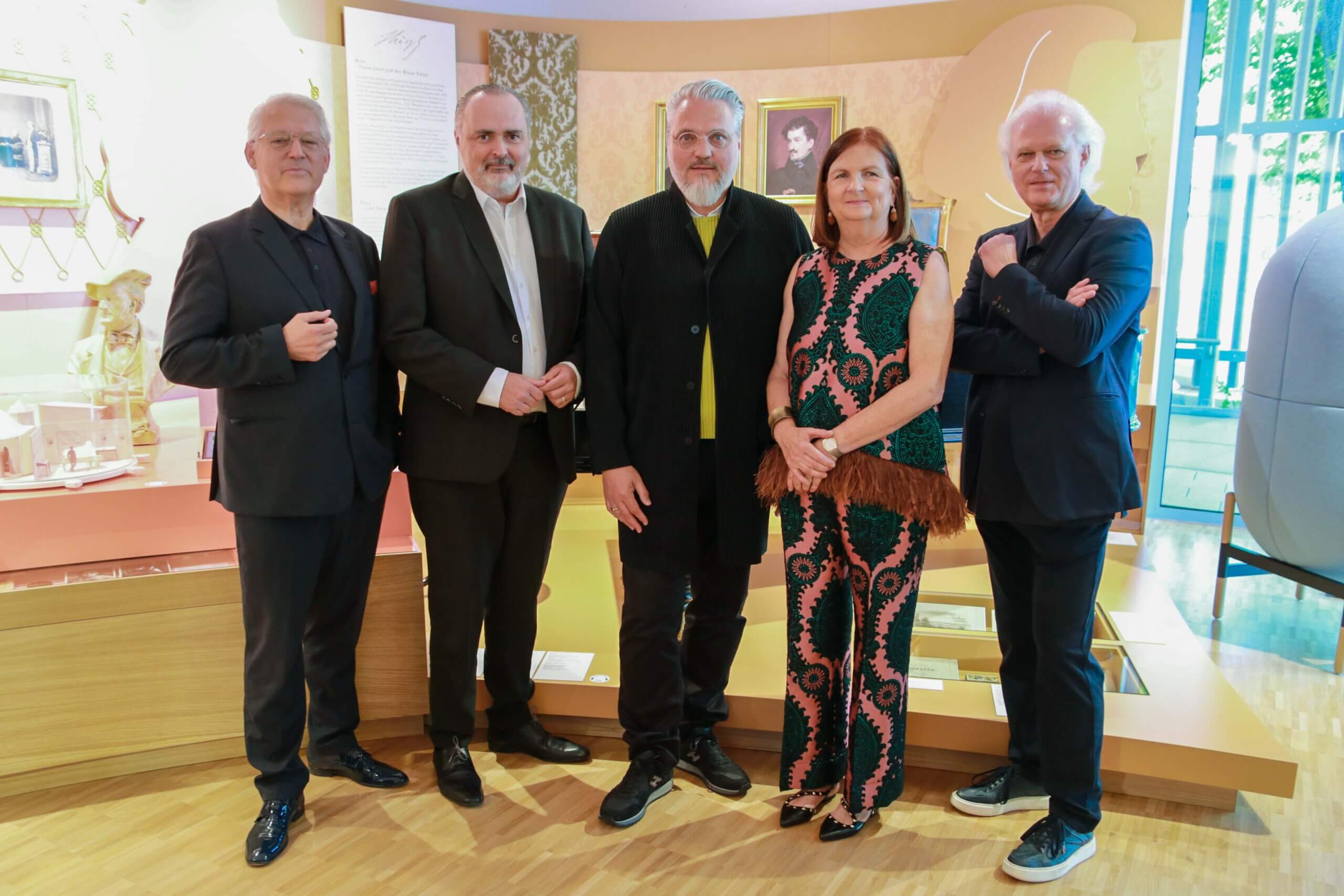 Gruppe von fünf Personen posiert in einem Museum vor einer Ausstellung, in stilvoller Kleidung.