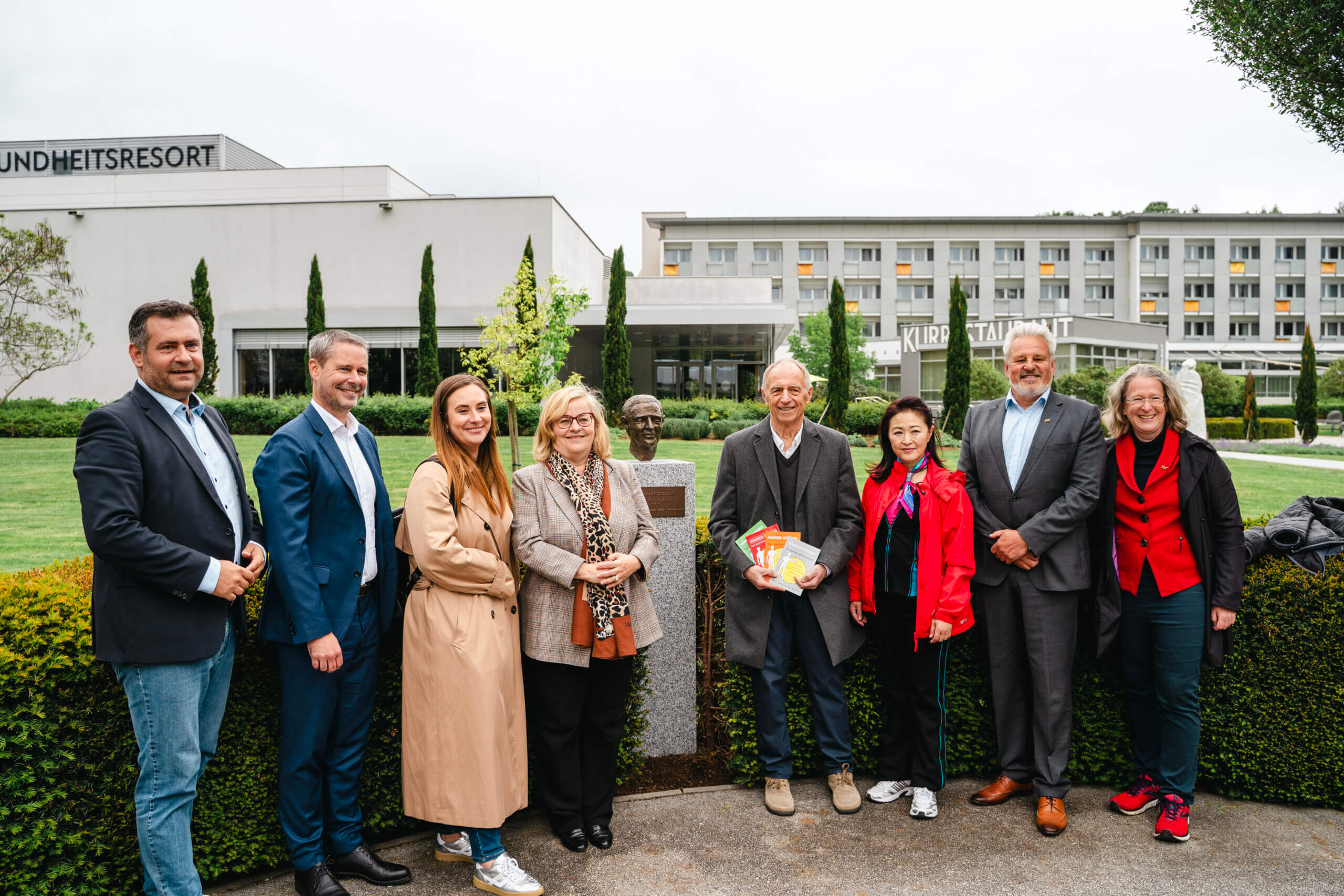 Gruppe vor Gesundheitsresort und Statue, Besucher und Team vereint für Wellness und Kultur im Freien.