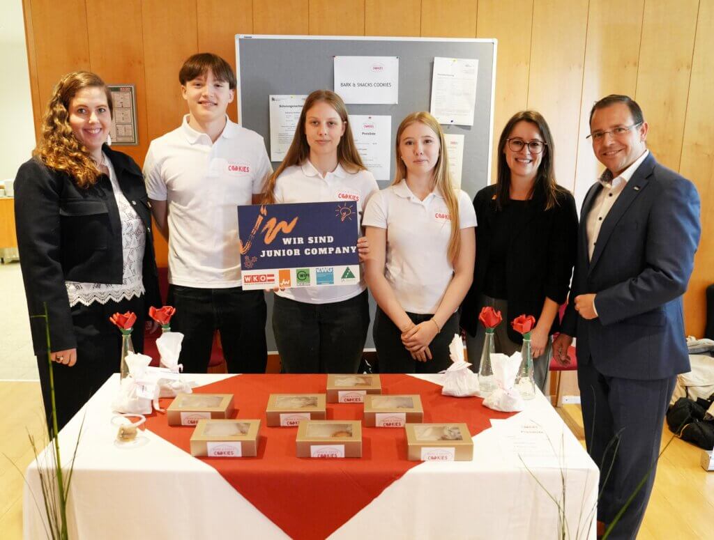 Team präsentiert Junior Company mit gebackenen Produkten auf Messe, neben Tisch mit Verpackungen und Dekoration.
