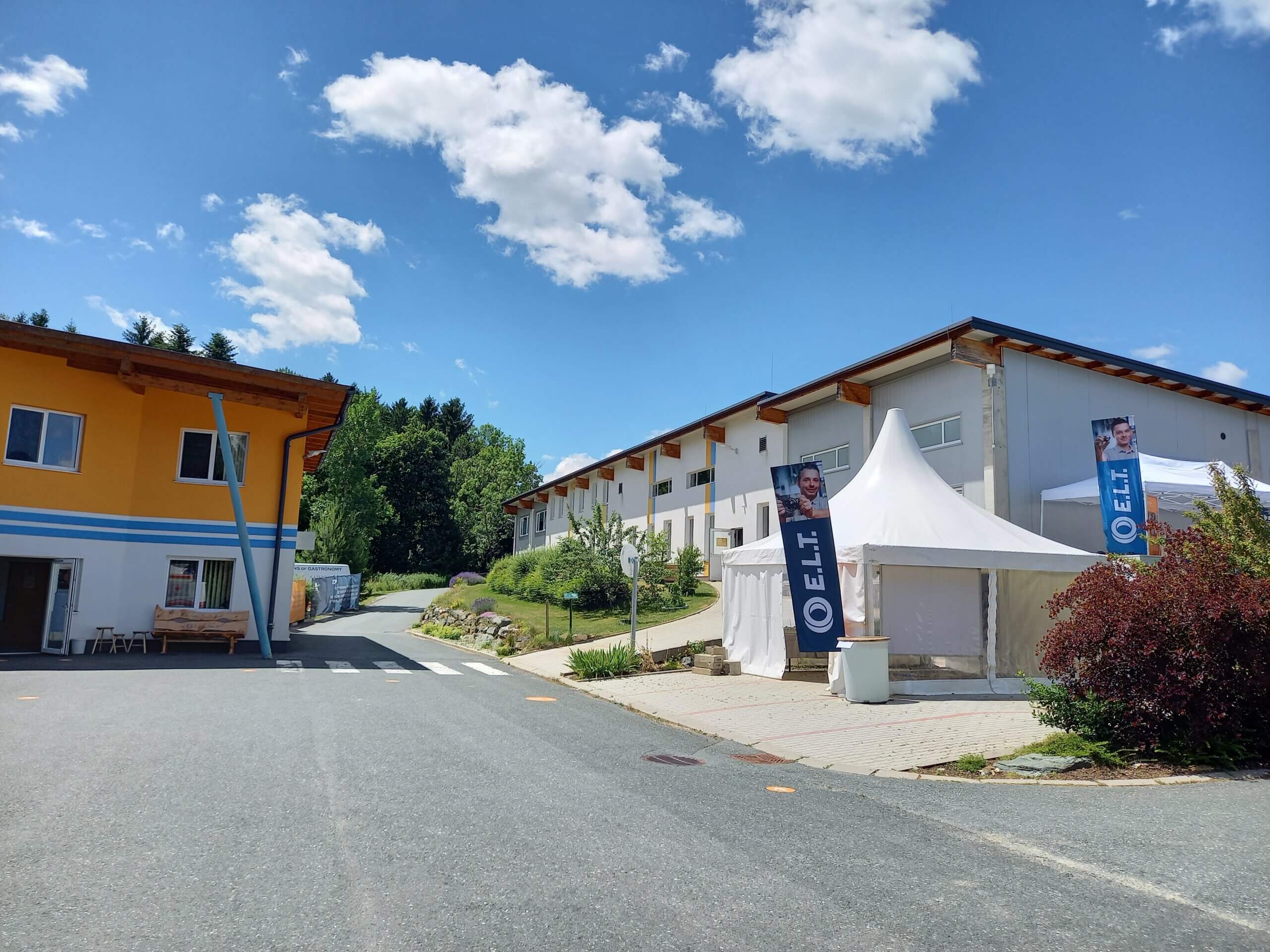 Moderne Firmengebäude mit Zelt und Werbebanner vor blauem Himmel in ländlicher Umgebung.