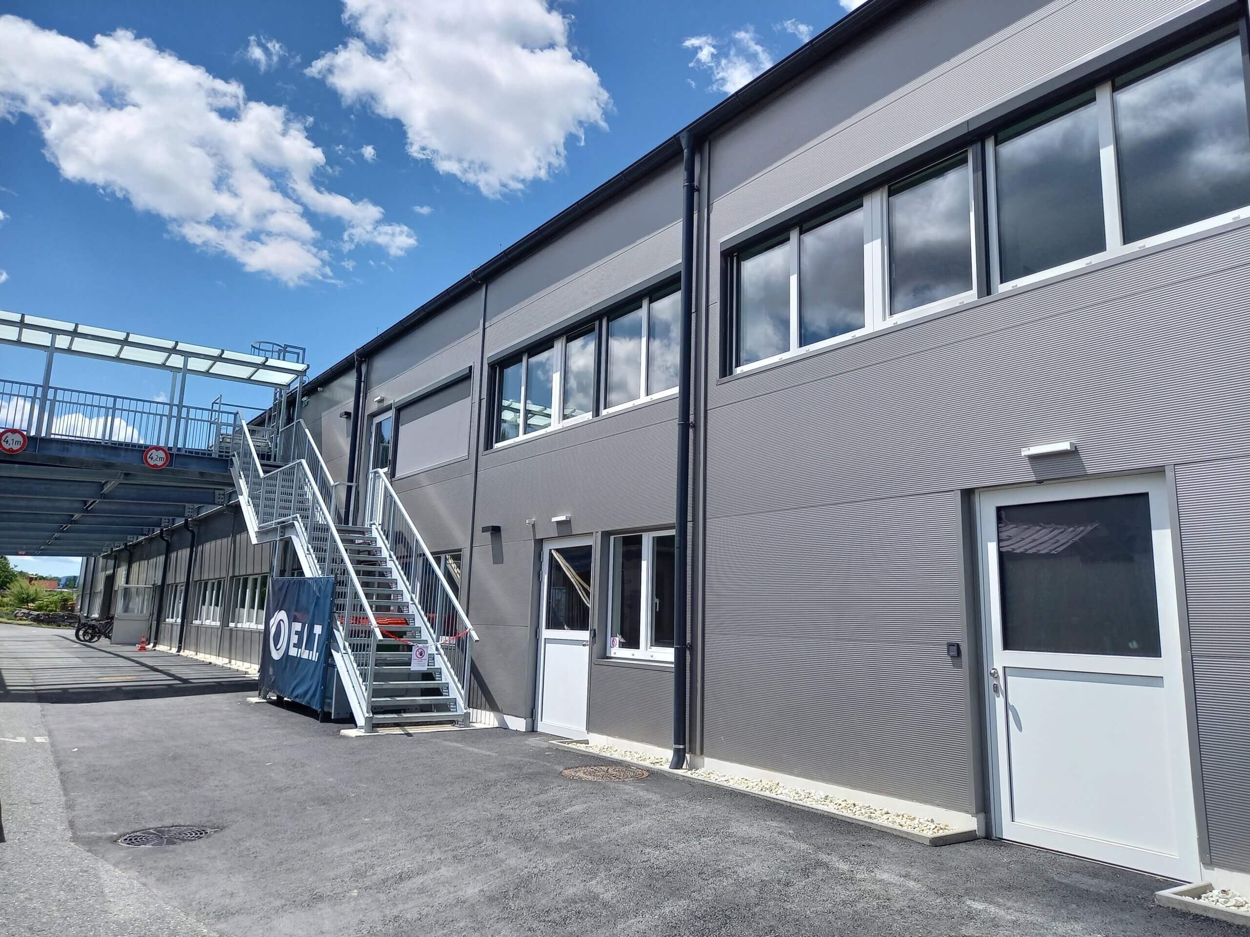 Moderne Bürogebäude-Fassade mit Treppenaufgang, klarem Himmel und Parkplatz im Vordergrund.