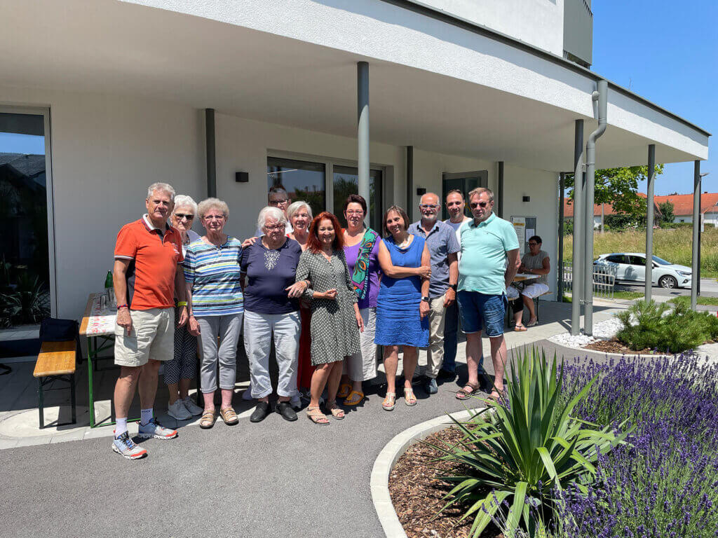 Gruppe von Menschen lächelt vor einem modernen Gebäude an einem sonnigen Tag. Gemeinschaft und Freude im Freien.