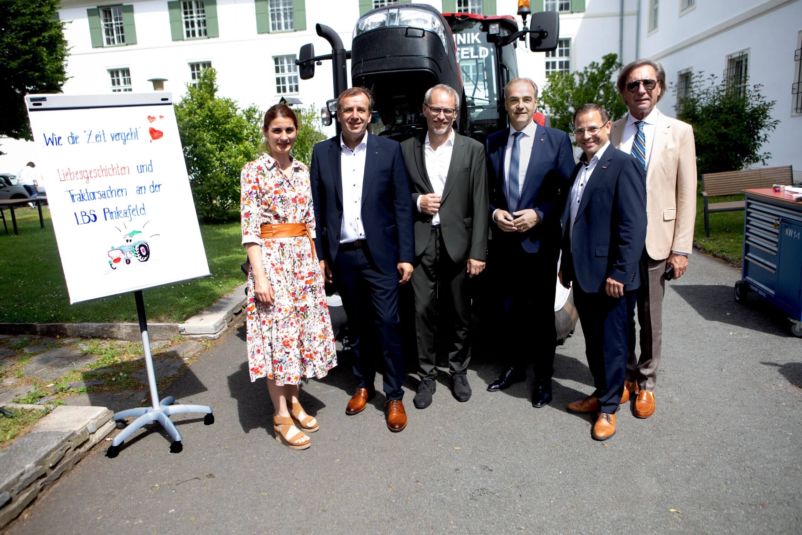 Personengruppe vor Traktor und Schild Wie die Zeit vergeht an der LBS Pinkafeld bei sonnigem Wetter.