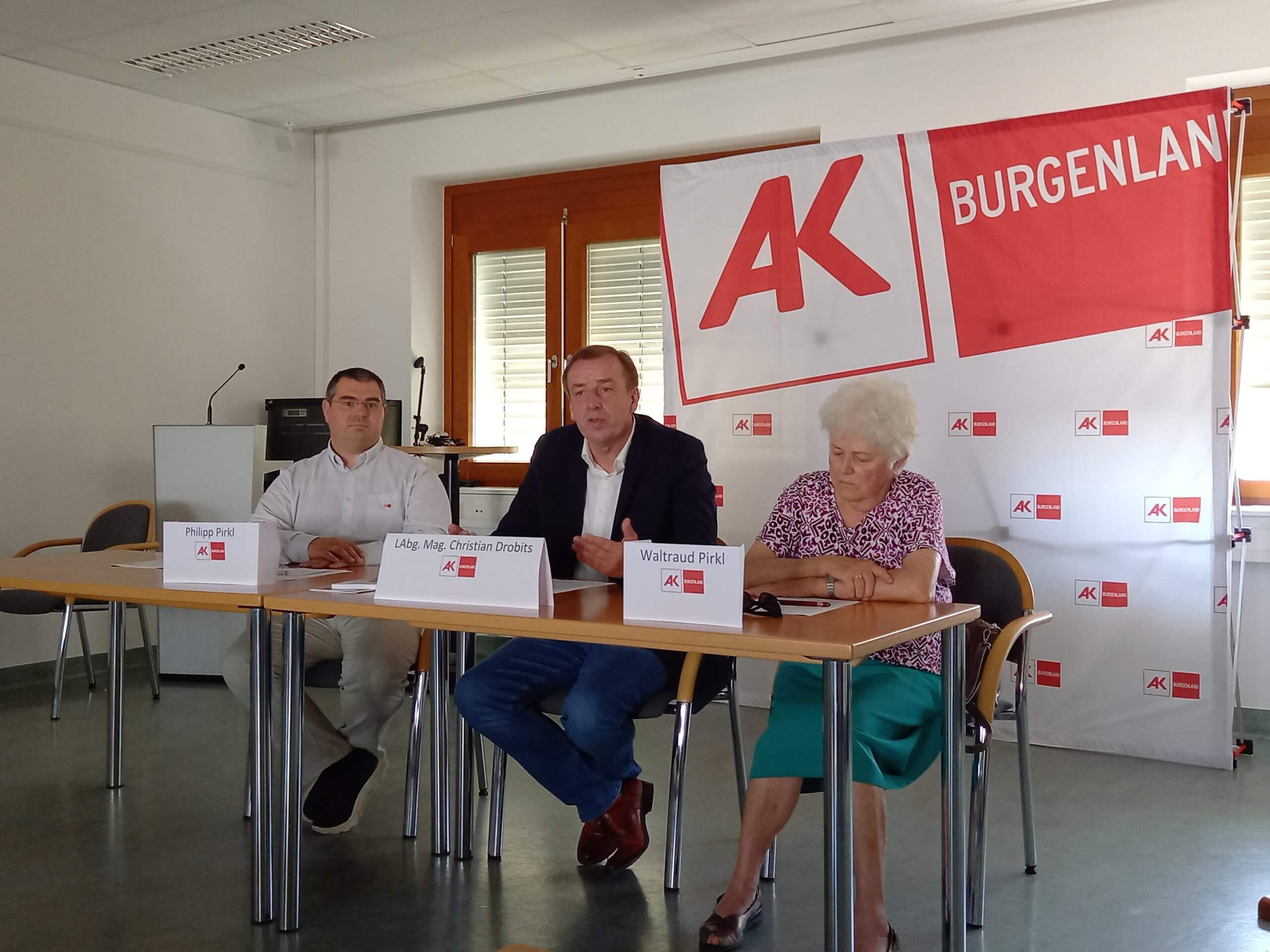 Drei Personen bei einer Pressekonferenz der Arbeiterkammer Burgenland, Banner im Hintergrund.