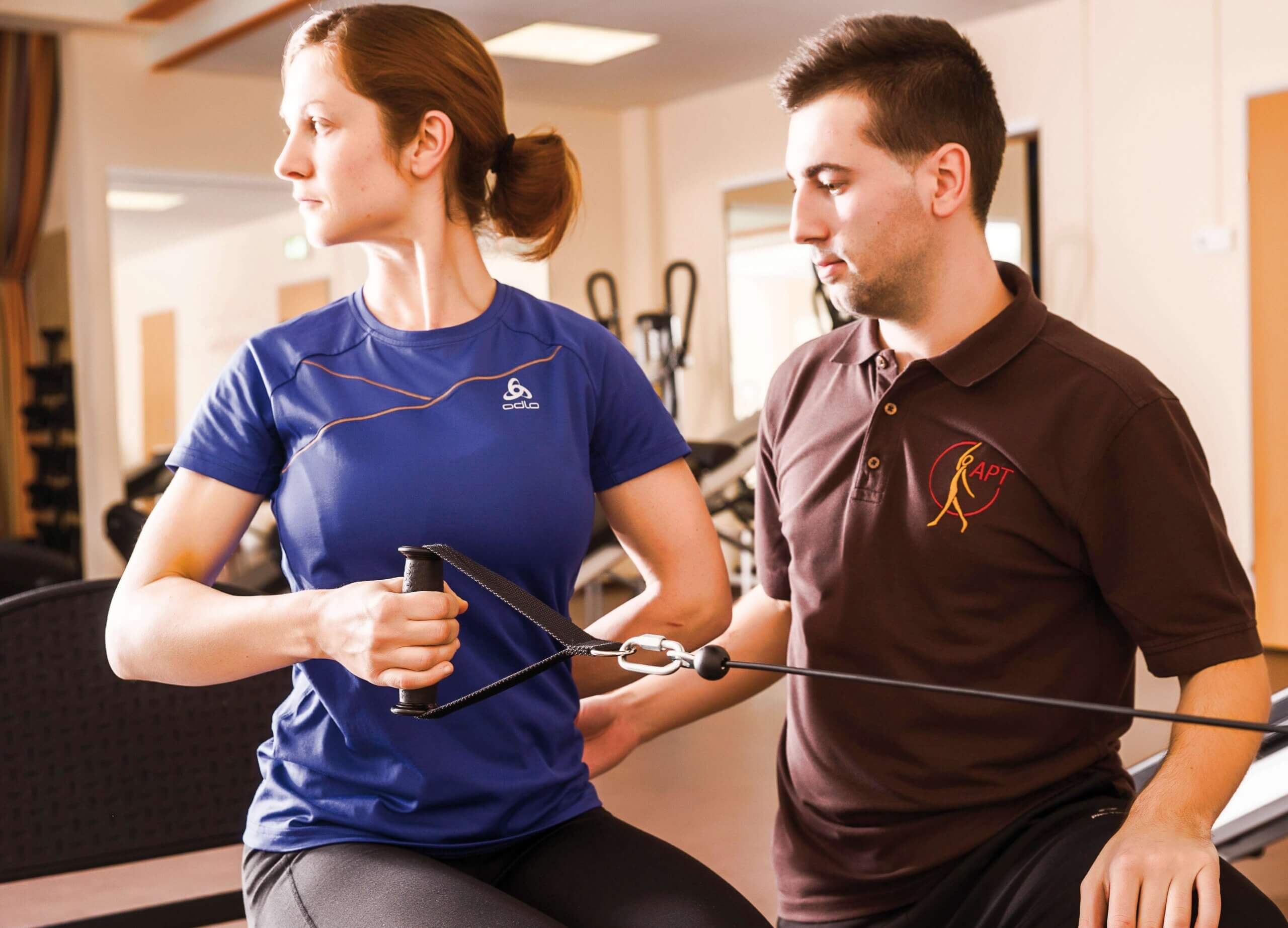 Fitness-Coach unterstützt Frau beim Training mit einem Zugseilgerät im Gym für optimale Gesundheit und Beweglichkeit.