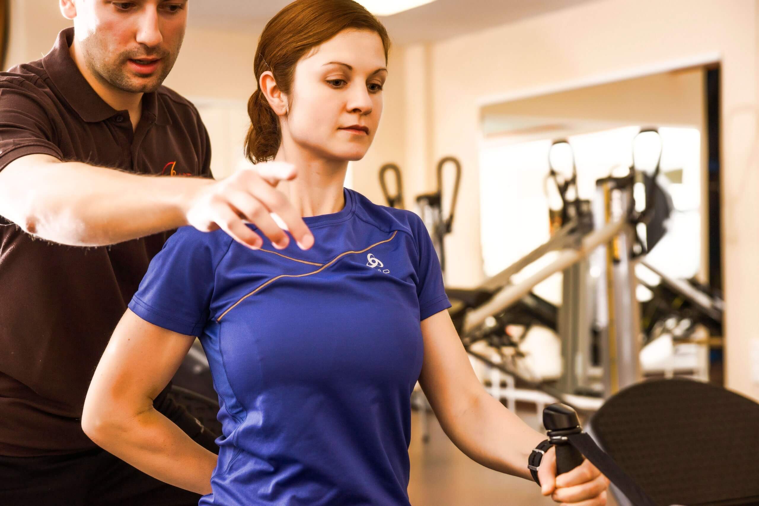 Trainer hilft Frau mit Fitnessübung im Gym, Fokus auf Bewegungsanleitung und Technik.