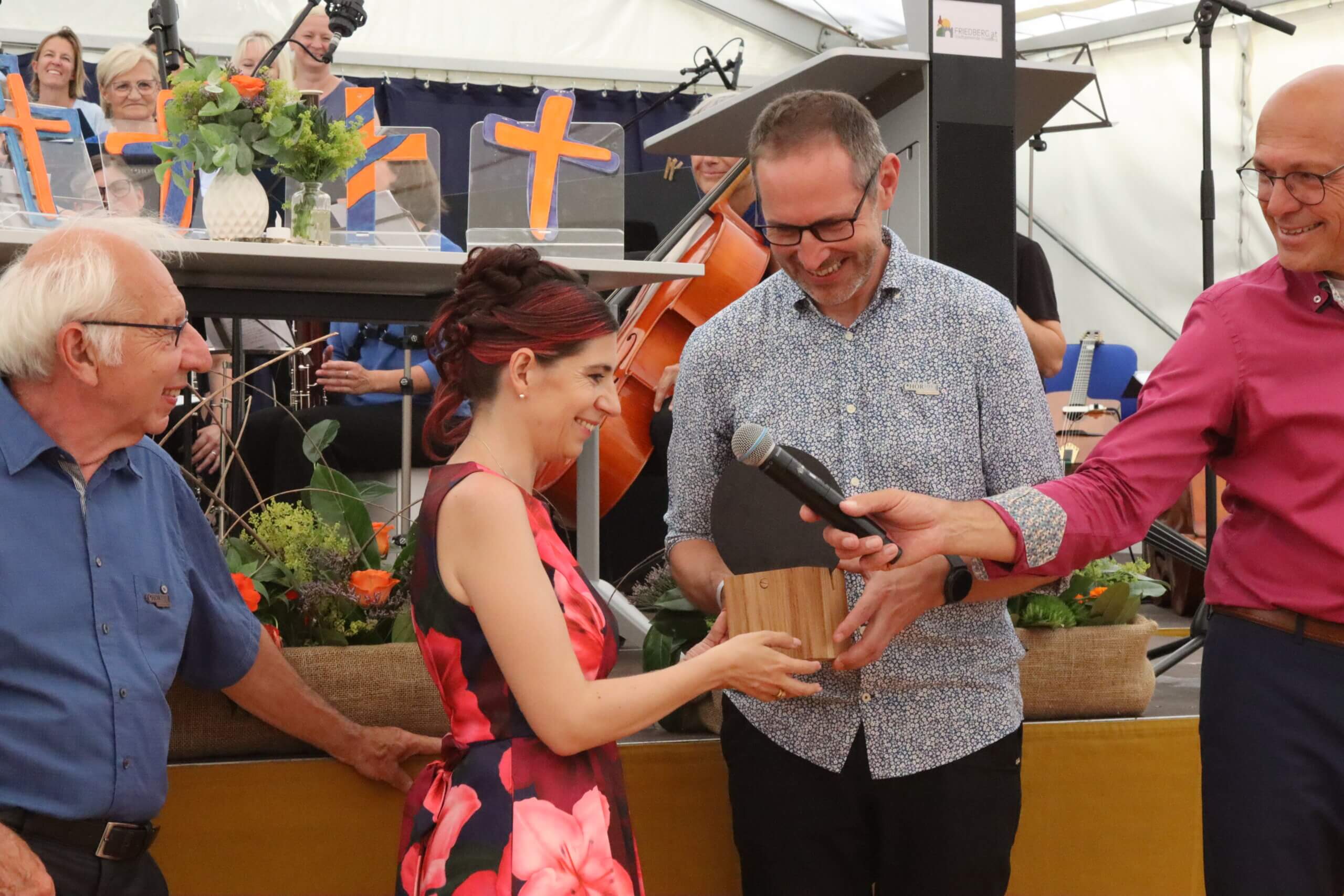 Glückliche Preisverleihung bei festlicher Veranstaltung mit lächelnden Teilnehmern und Blumen im Hintergrund.
