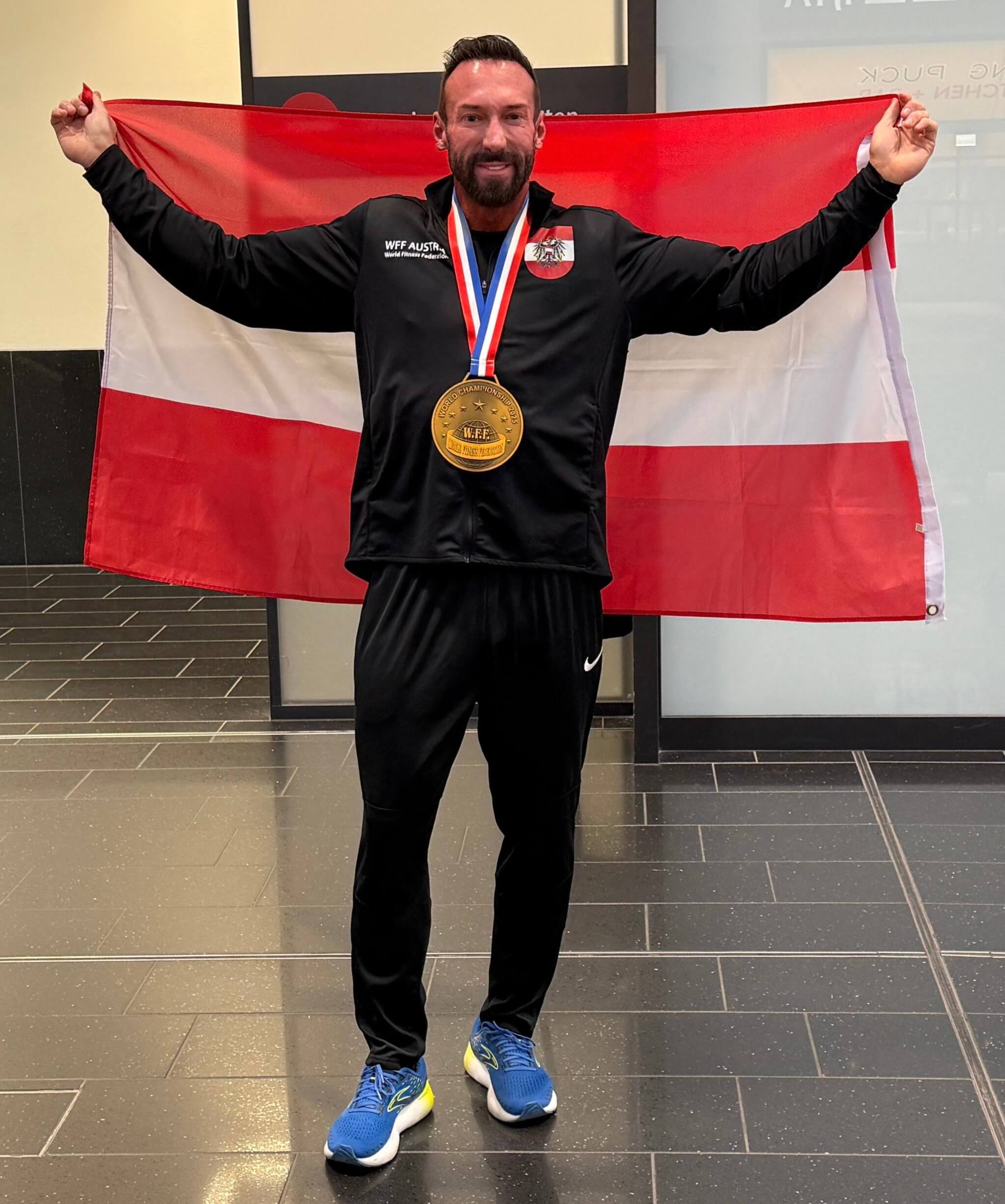 Person mit Medaille und Österreich-Flagge feiert Erfolg in Sporthalle.